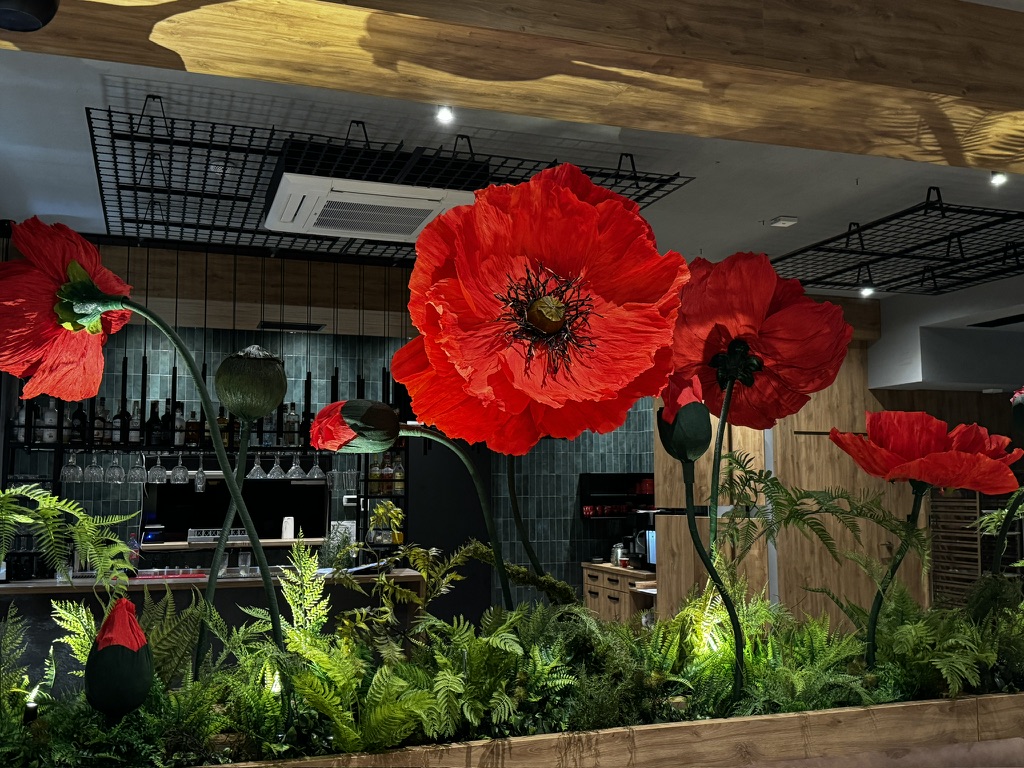 Indoor decorative large red poppies with green ferns in a wooden planter in a modern bar setting.