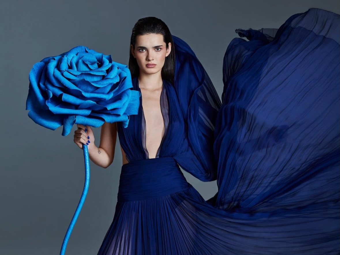 Sesja zdjęciowa Top Model. Modelka w granatowej sukni trzymająca artystyczny, niebieski kwiat gigant Fiori di Matis