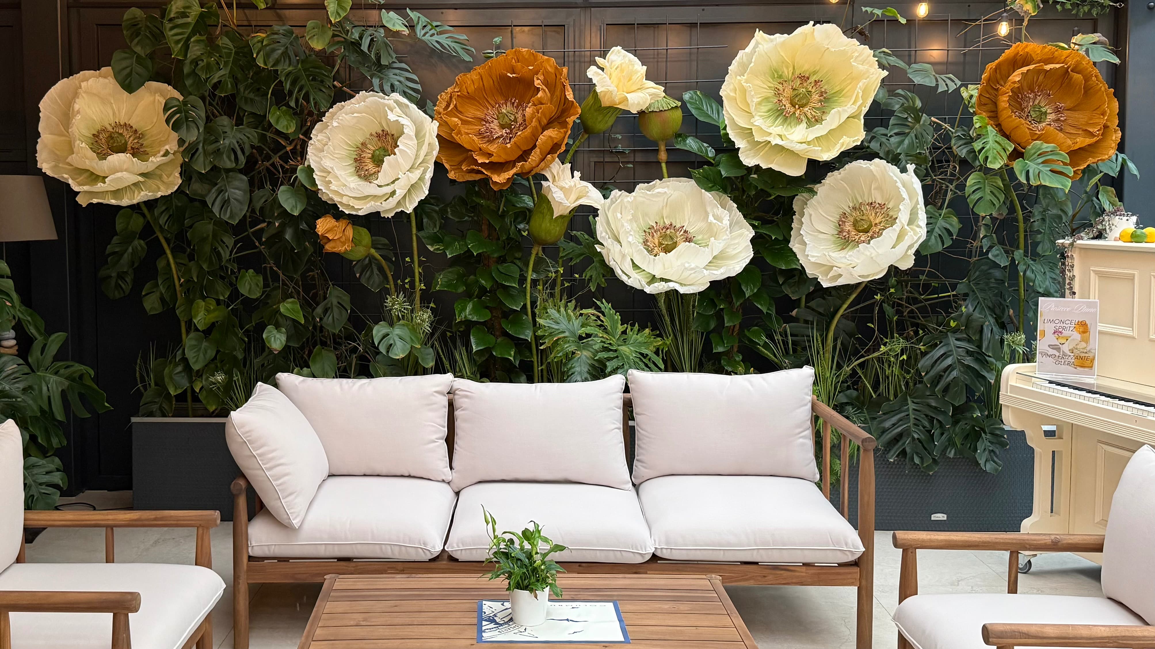 Wood-framed sofa and chairs with white cushions in front of large decorative cream and orange flowers.