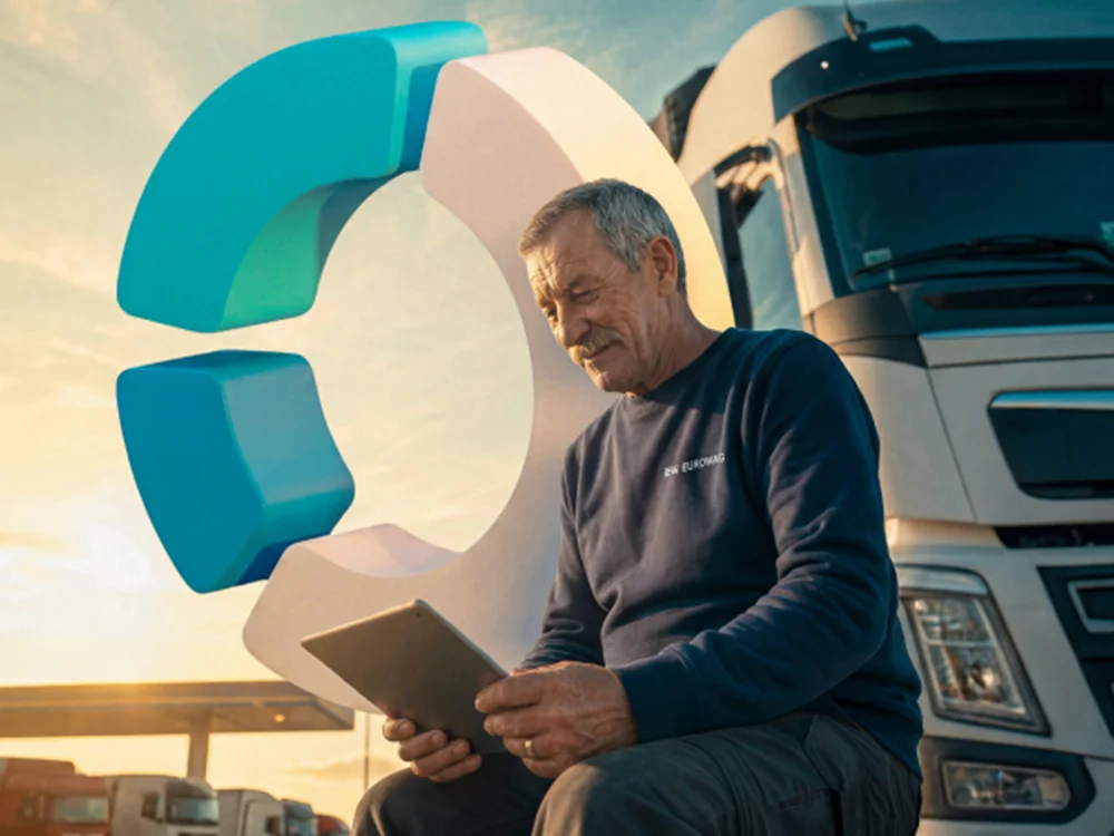 Man in navy sweatshirt sitting near a truck, using a tablet, with a large 3D geometric logo behind him.