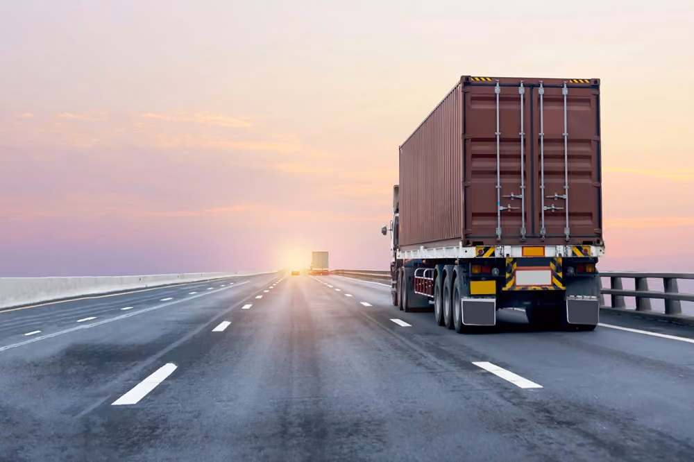 A truck driving down a road toward the horizon, surrounded by open landscape.