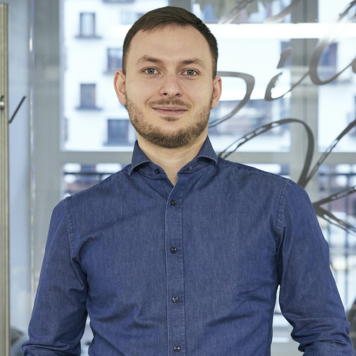 A man in a blue shirt standing in front of a window.