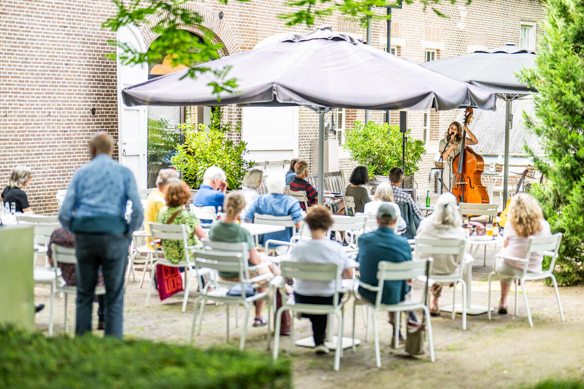 Het terras van Kasteel het Nijenhuis. Mensen zitten op witte stoelen buiten onder parasols.