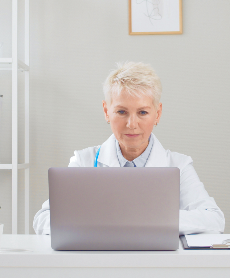Uma mulher de cabelos curtos e brancos vestida de jaleco branco e mexendo em um notebook