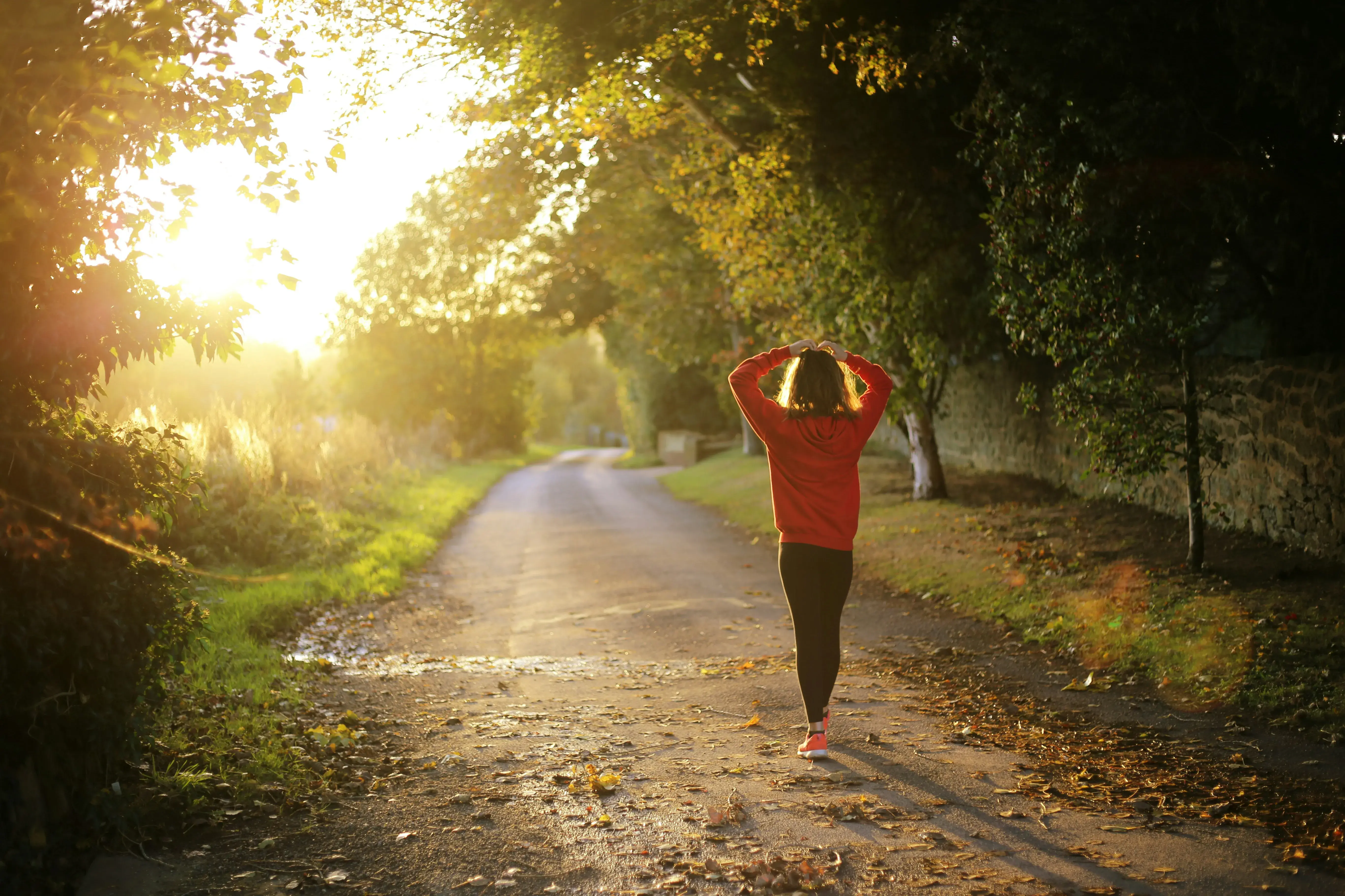 Femme marchant sur un chemin bordé d’arbres au lever du soleil, illustrant la déconnexion, la nature et le ressourcement lors d’un séjour bien-être.