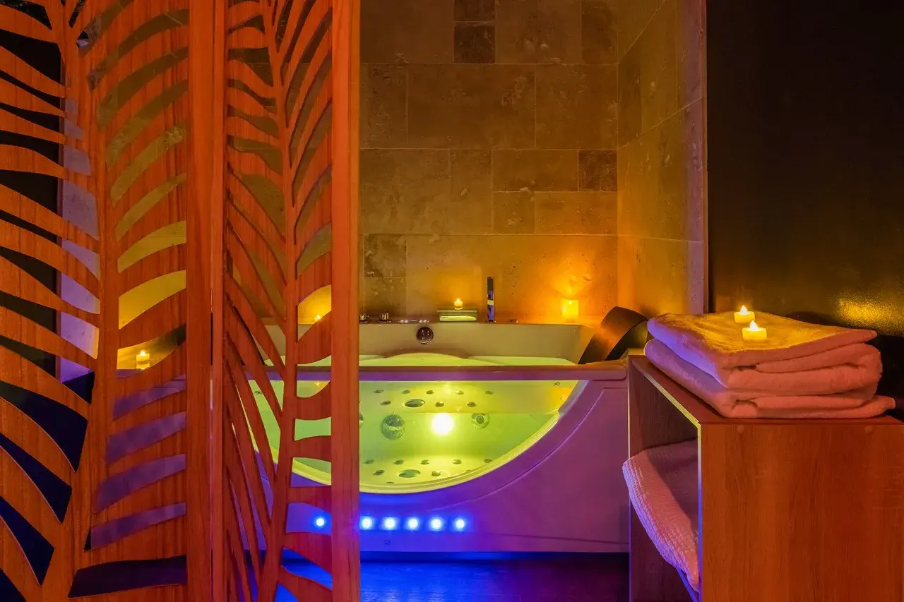Illuminated whirlpool bath in OIQIA’s Jungle Room in Narbonne, featuring exotic décor and soft lighting for a romantic getaway with a private jacuzzi.