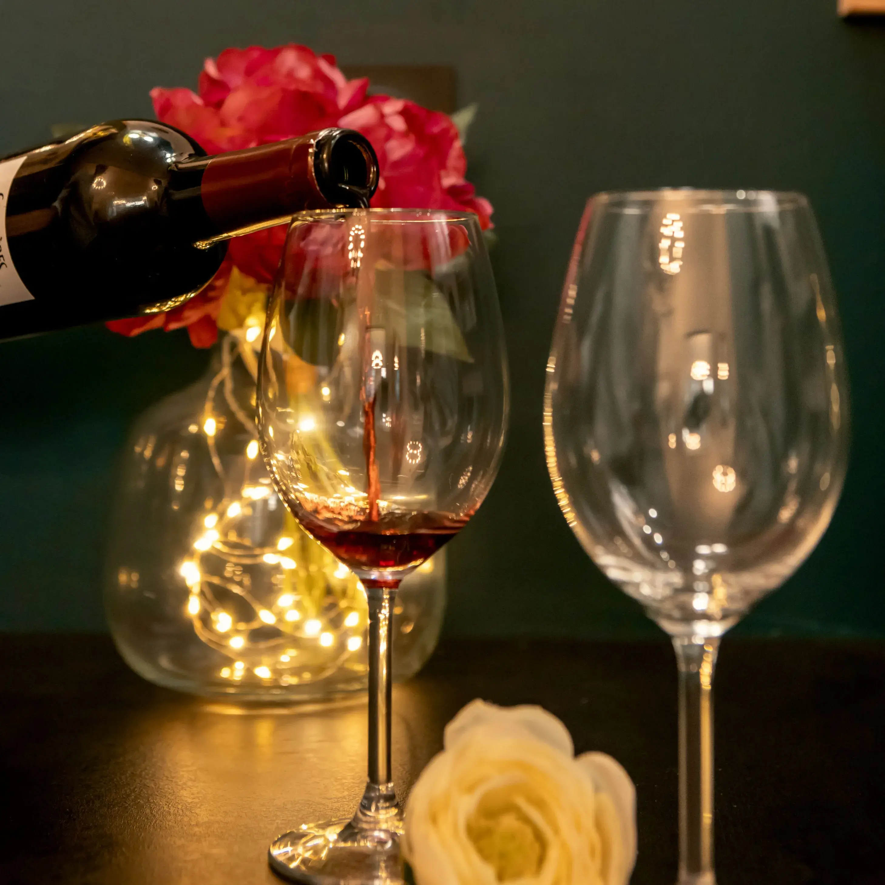 Two glasses of red wine being poured by candlelight, creating a warm and romantic atmosphere in an OIQIA love room in Narbonne.