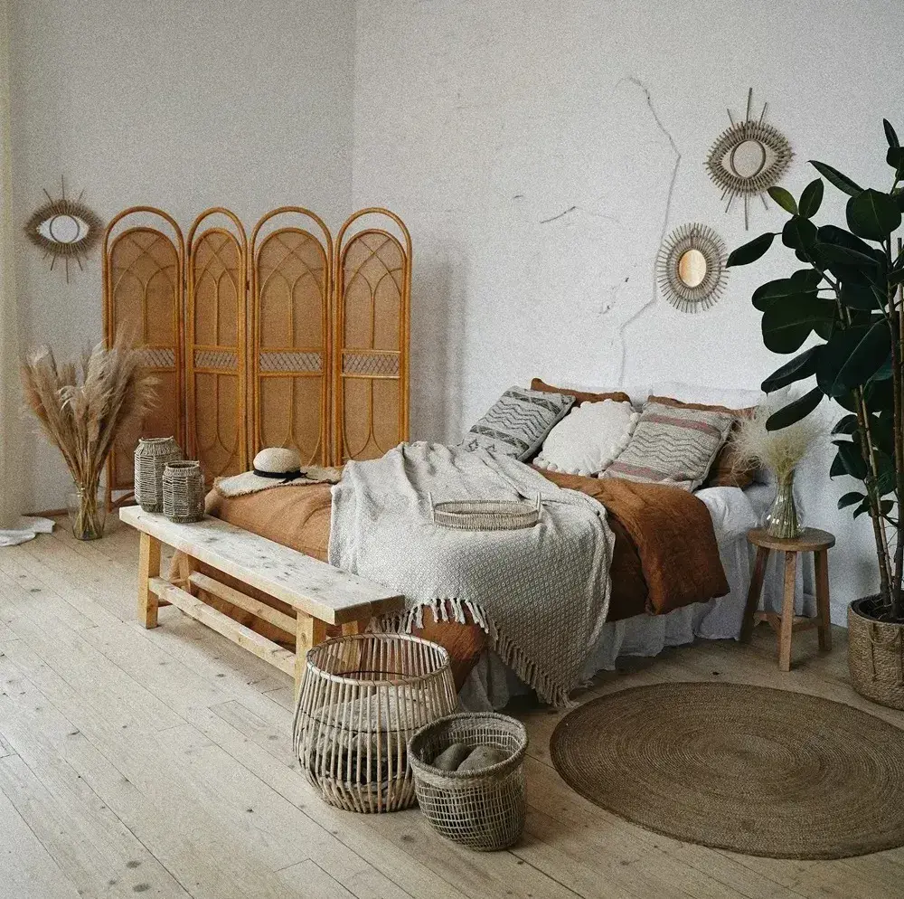 Chambre décorée dans un style bohème avec paravent en rotin, paniers en fibres, literie texturée et plantes vertes.