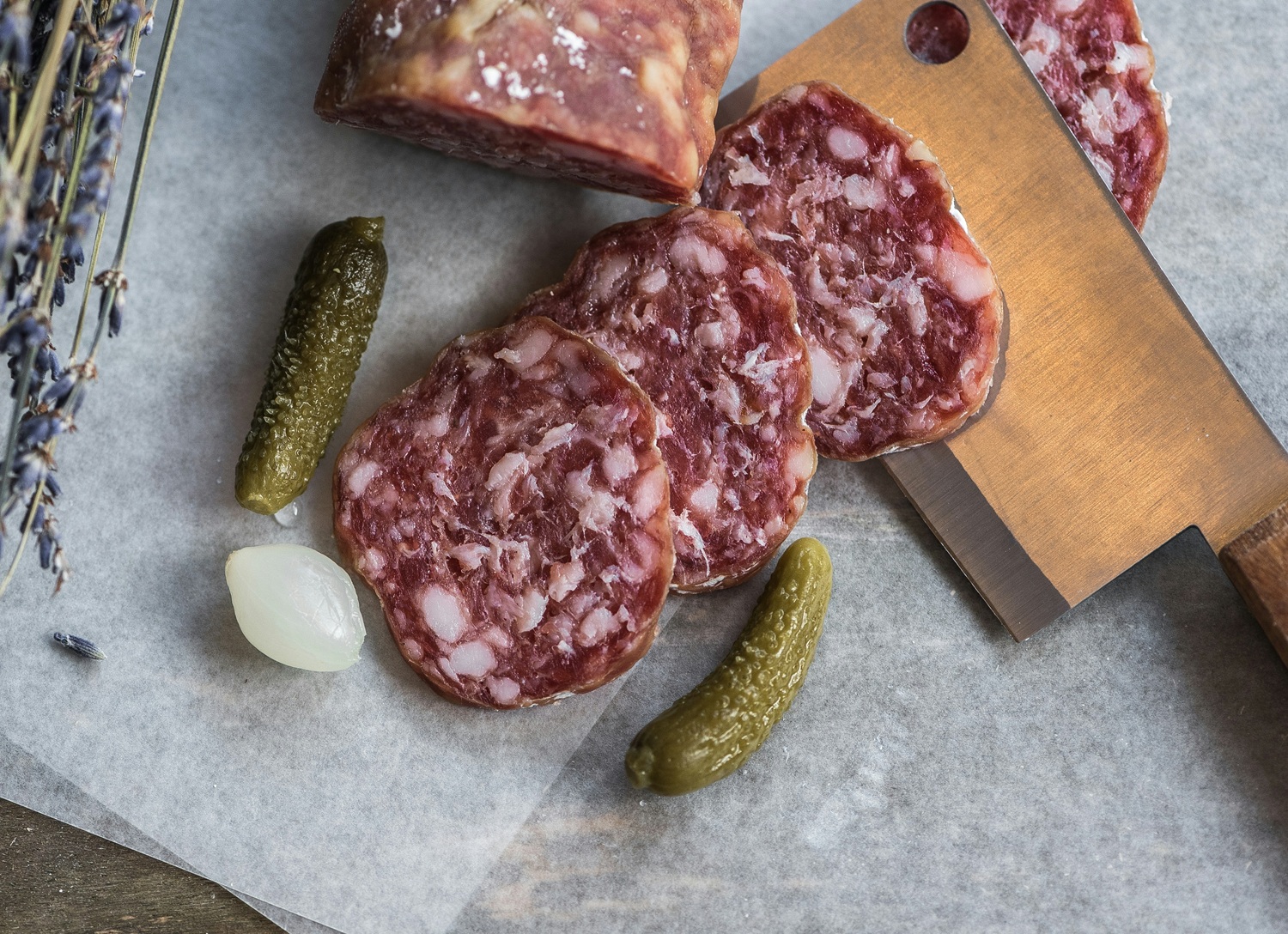Assiette de saucisson et cornichons typiques du Beaujolais, coupés sur une planche rustique, parfaite pour accompagner un verre de Beaujolais nouveau.