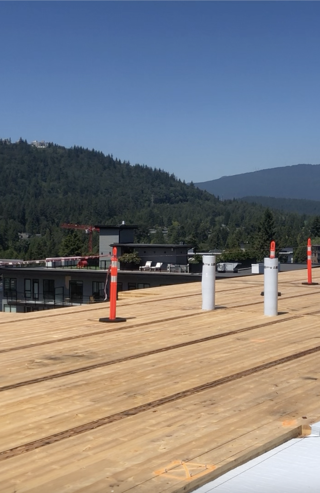A wooden rooftop deck with several white and orange safety posts, overlooking a green mountainous landscape under a clear blue sky. This image represents roof installation in Coquitlam, showcasing an active construction site.