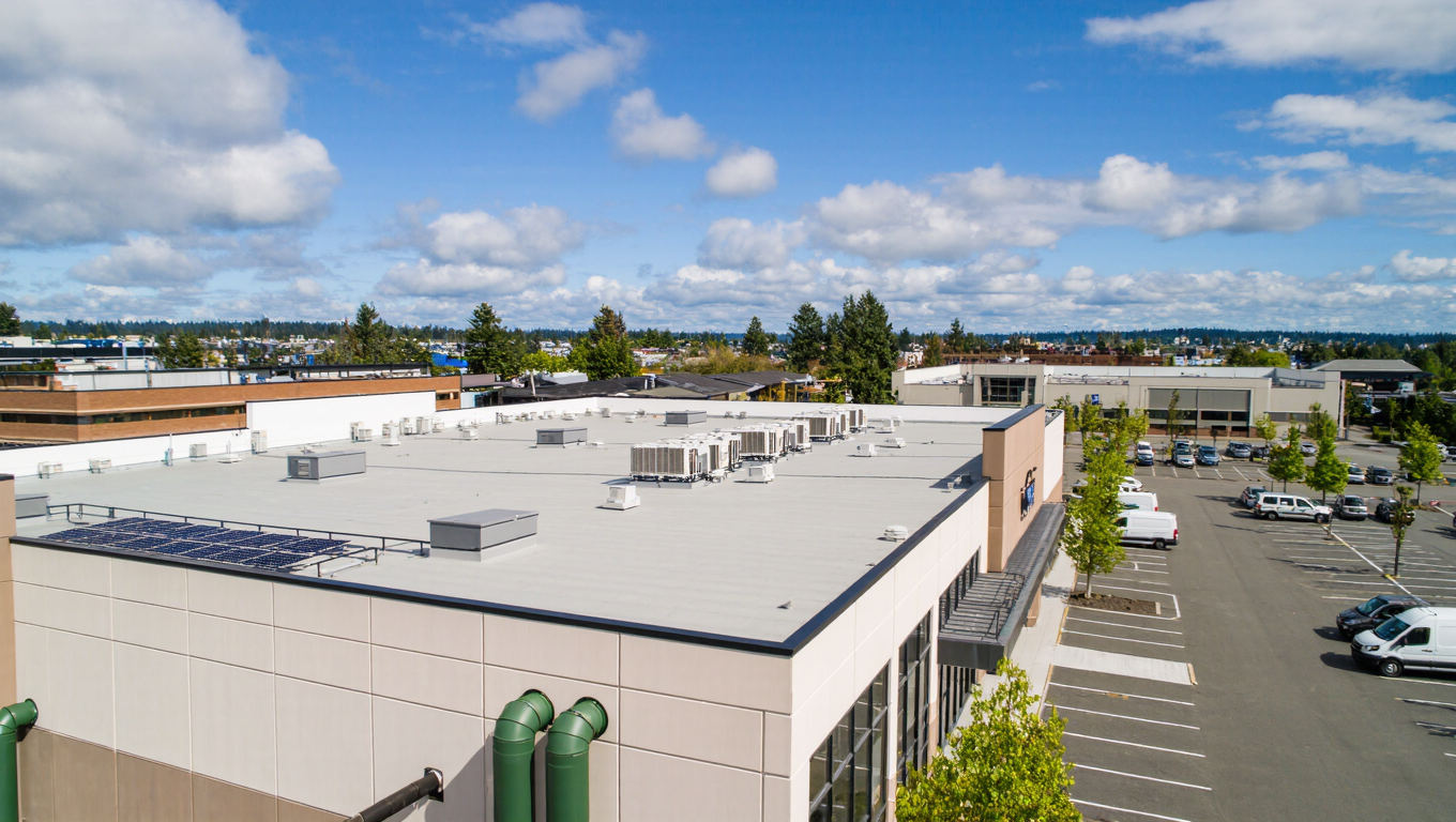 An aerial view of a commercial building roof in Richmond BC, featuring air conditioning units, surrounded by a parking lot and several trees under a partly cloudy sky.