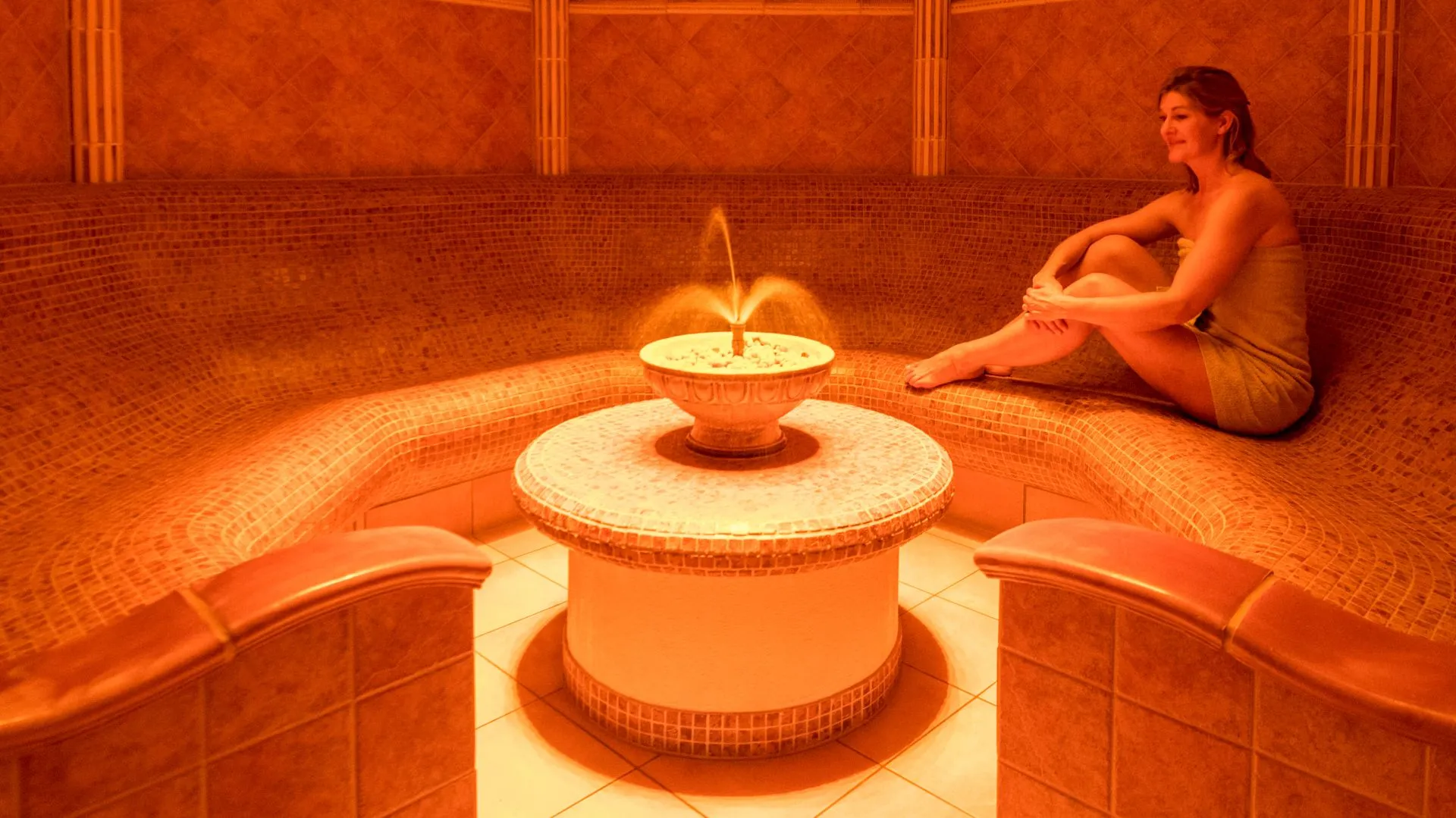 Warm hammam interior with fountain and person relaxing in orange light
