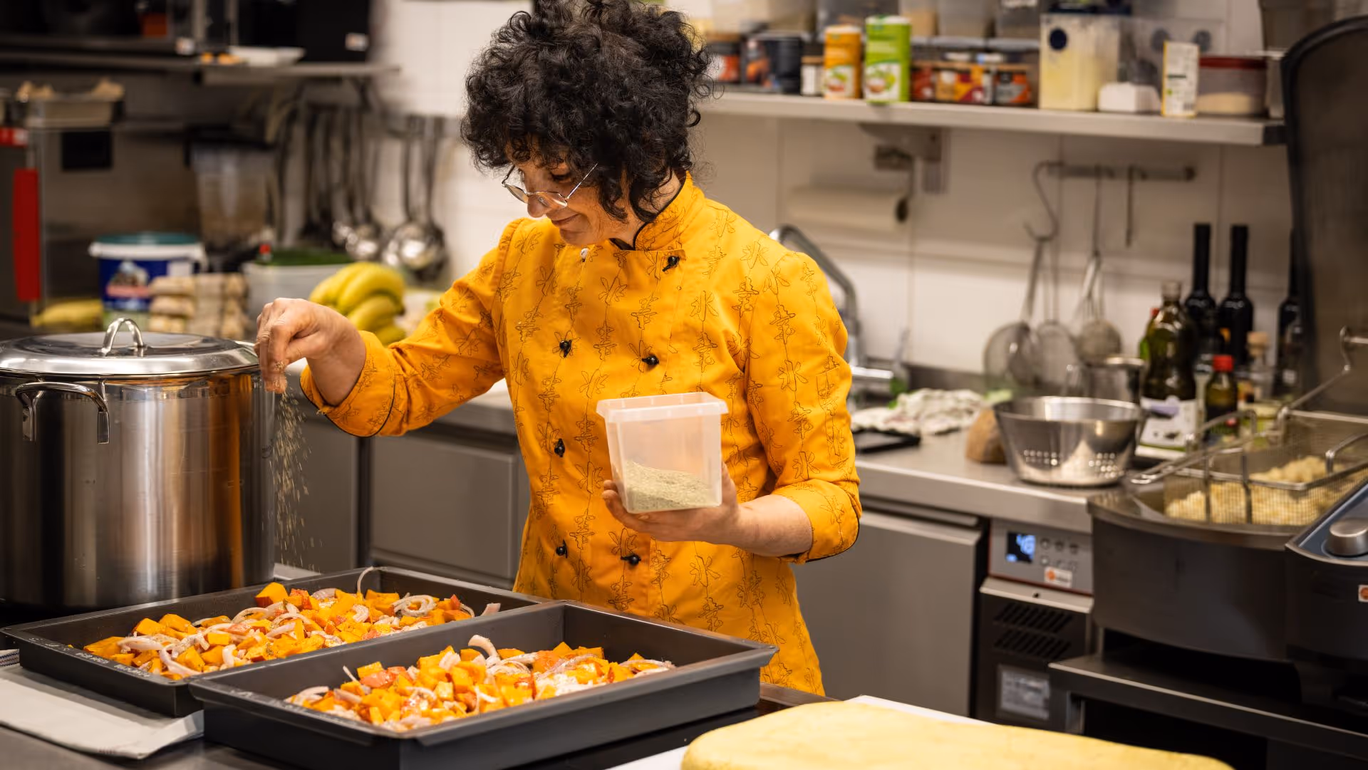 Koch in gelber Jacke würzt Gemüse in der Küche mit Gewürzen