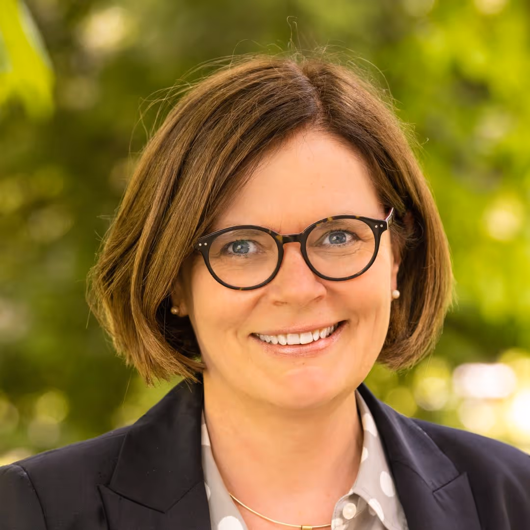 Professional woman smiling in glasses and black blazer, green background