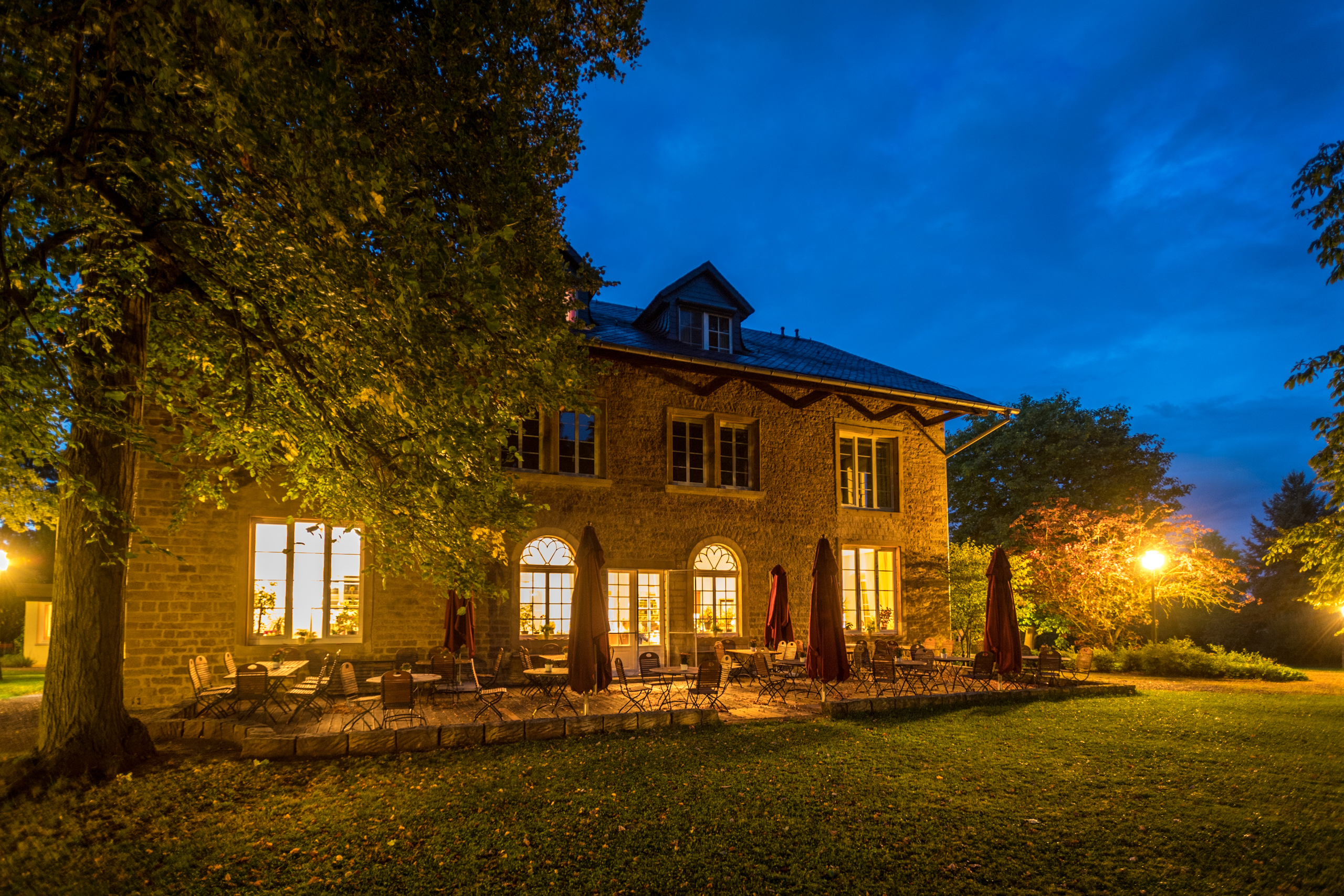 Beleuchtetes Steinhaus mit Außenterrasse in nächtlicher Gartenstimmung