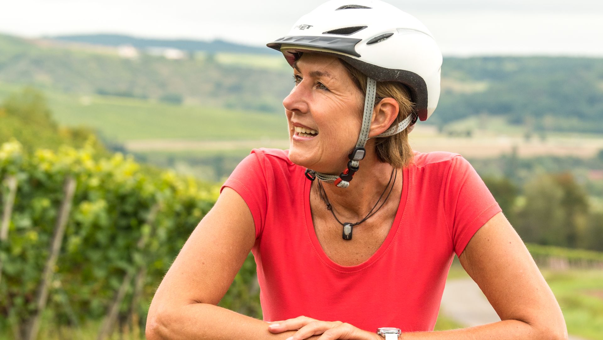 Lächelnde Radfahrerin mit weißem Helm in grüner Landschaft