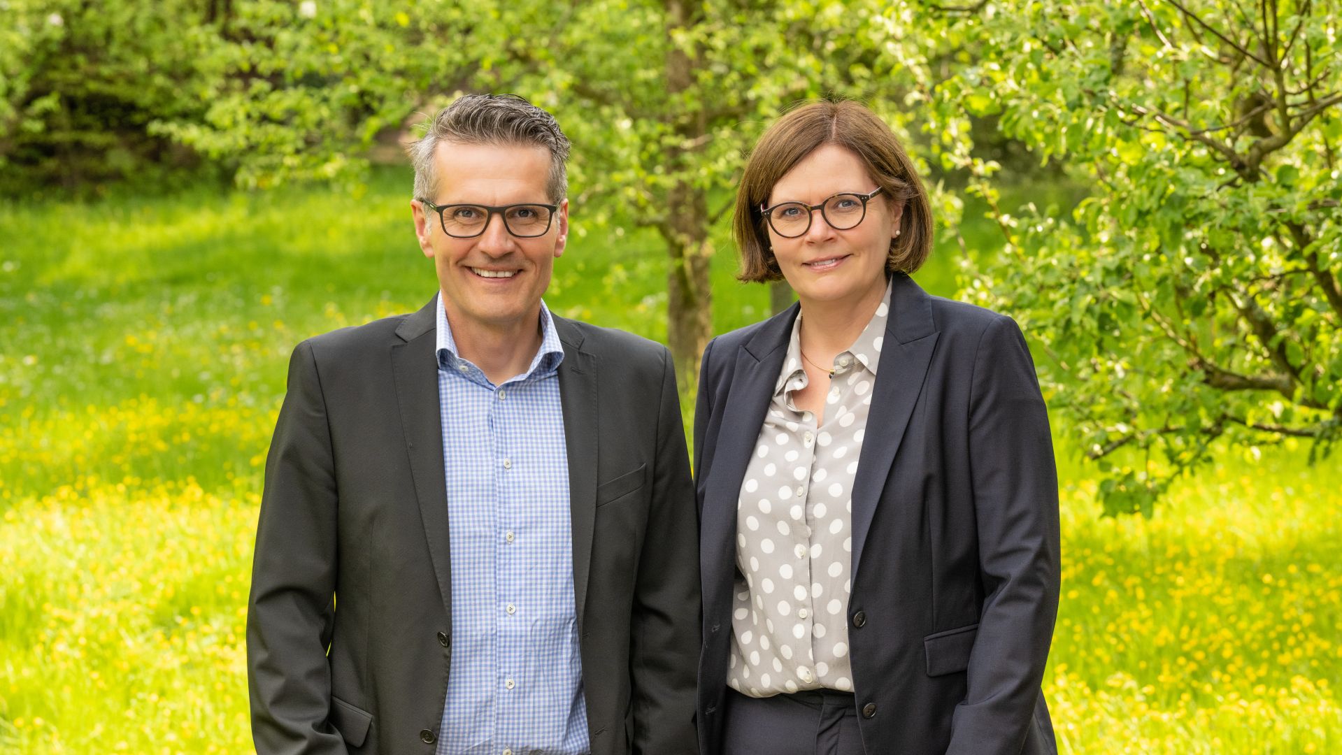 Zwei Geschäftspartner lächeln im Freien vor grünem Blätter-Hintergrund