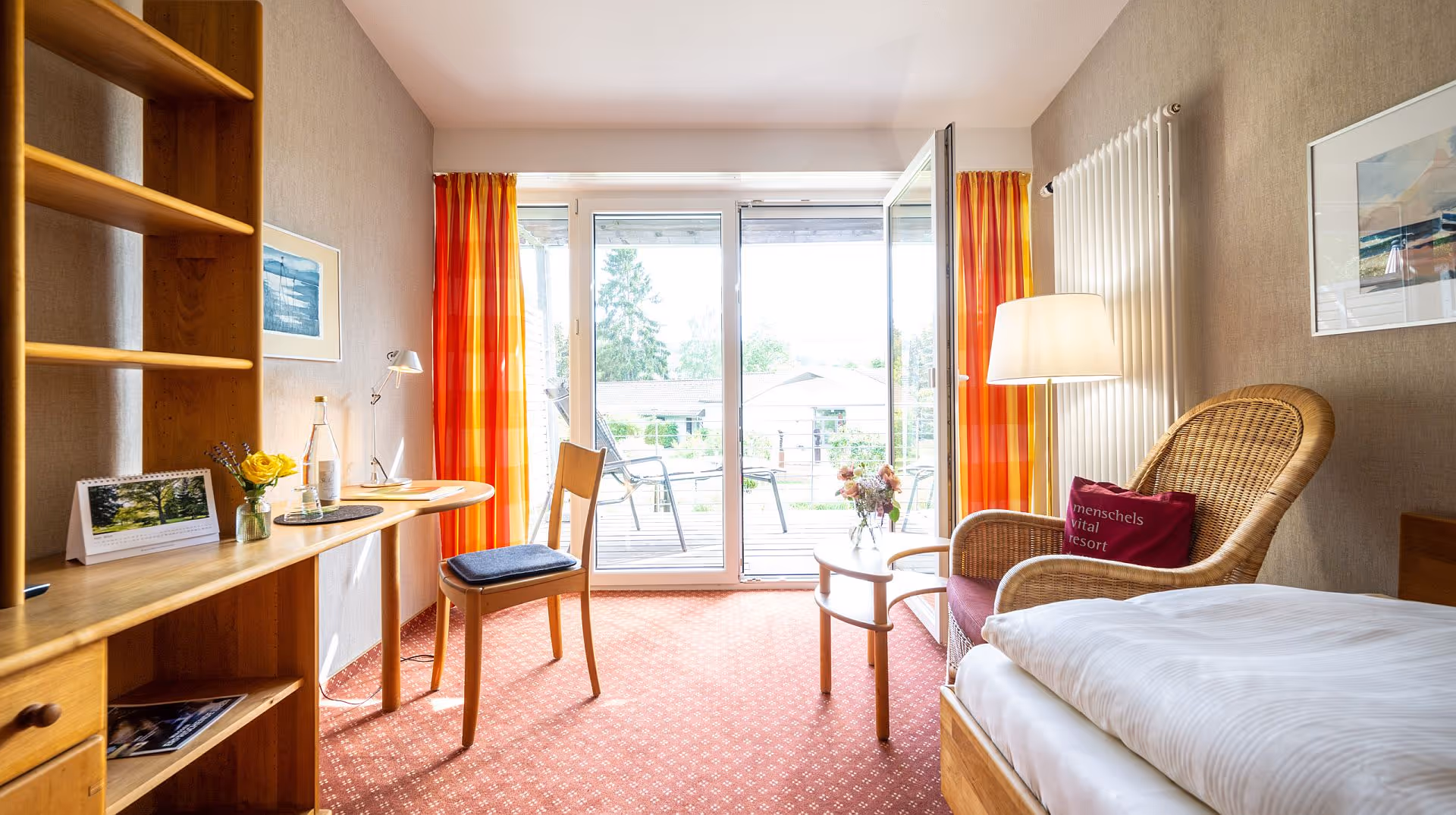 Cozy hotel room with red carpet, wicker chair, and large windows