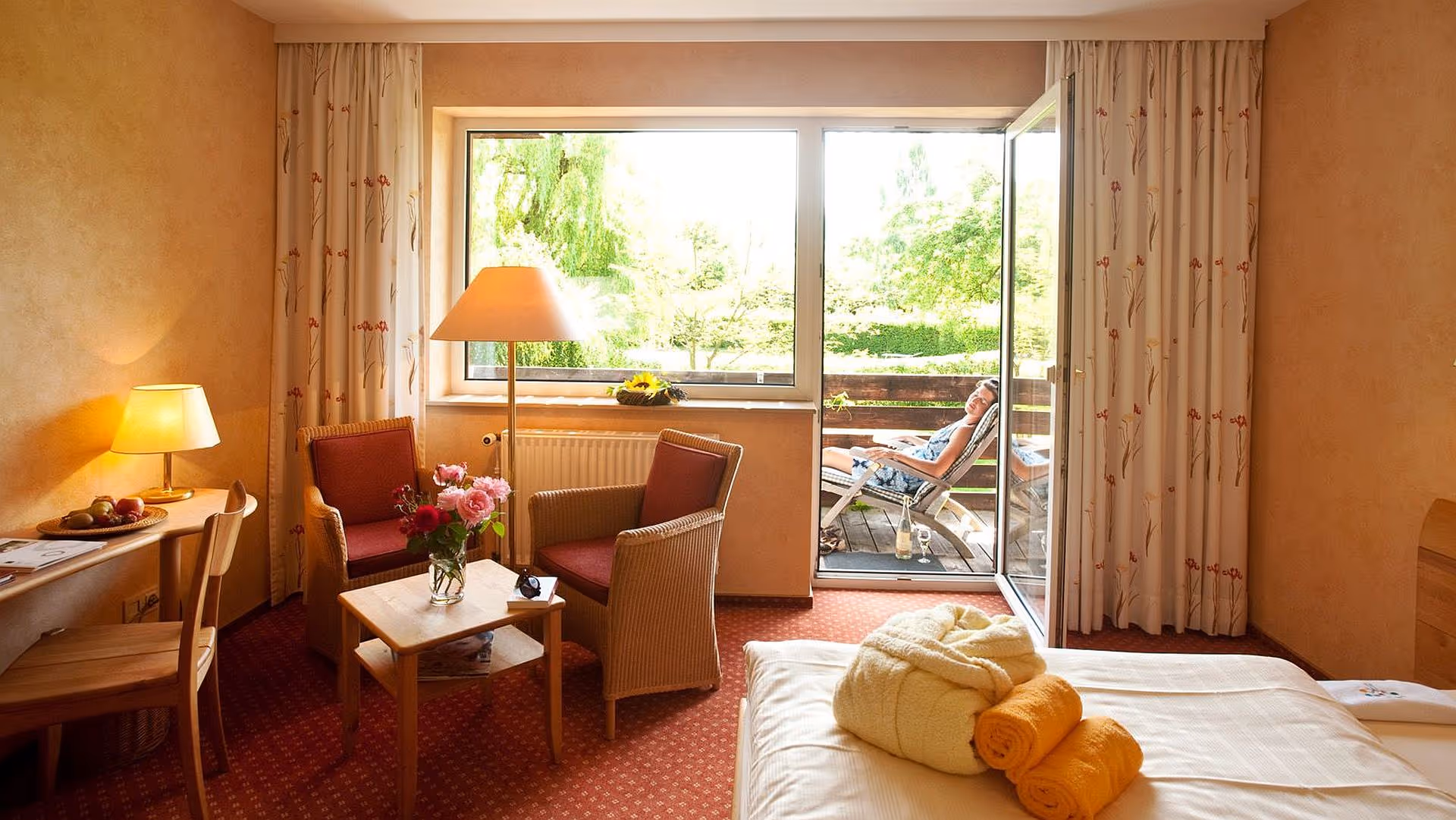 Cozy hotel room with sitting area, flowers, and balcony overlooking garden