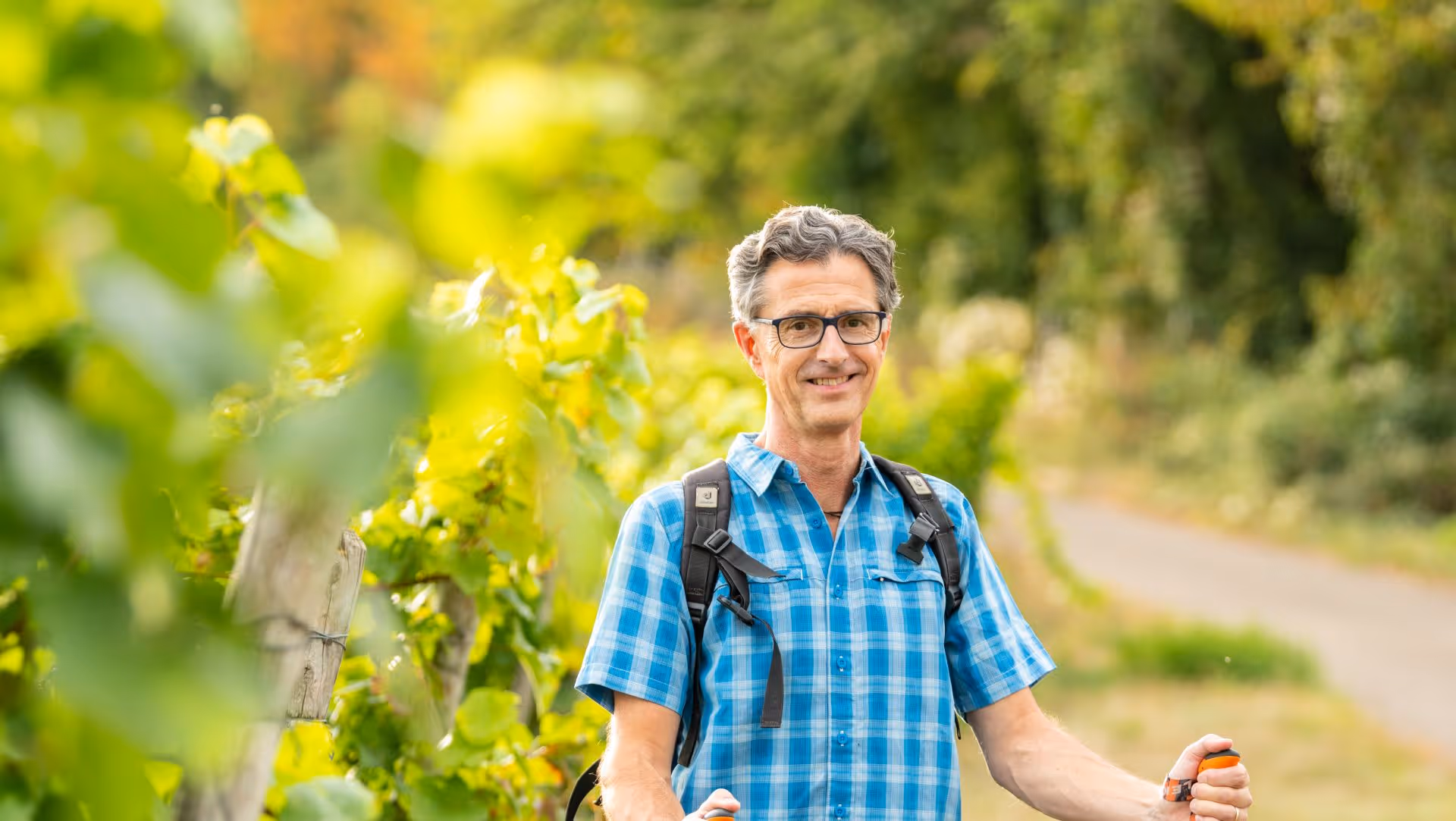 Lächelnder Wanderer mit Rucksack auf einem Weinbergweg im Sommer