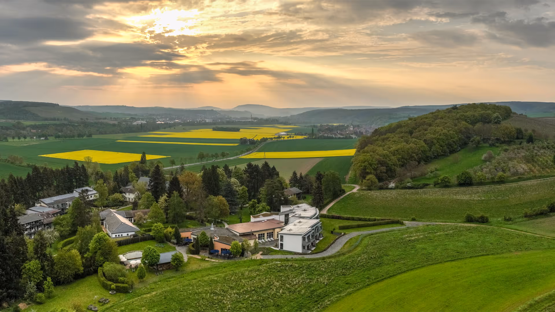 Scenic countryside landscape with yellow fields, green hills, and sunset sky