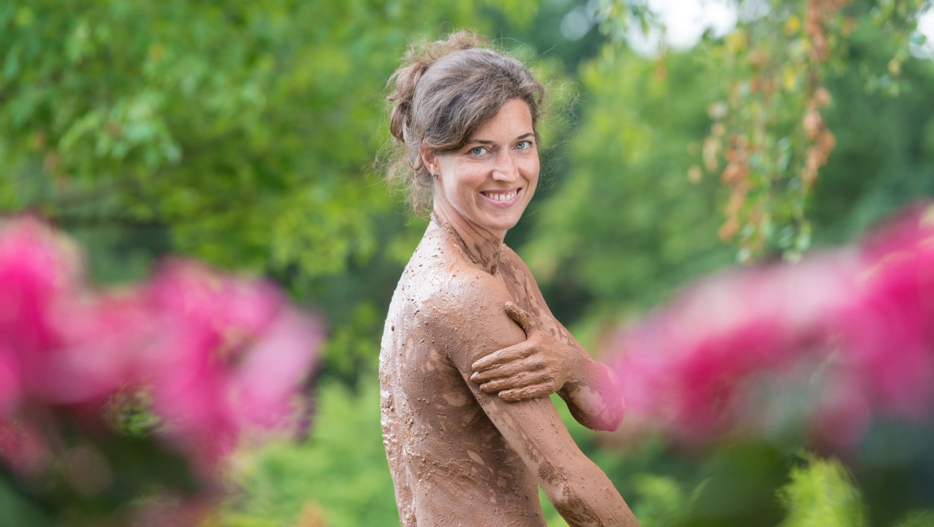 Lächelnde Person mit Lehm bedeckt, umgeben von Blumen und Grün