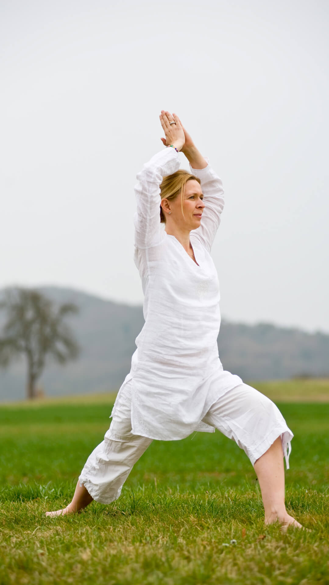 Woman in white practicing yoga pose outdoors on grassy field