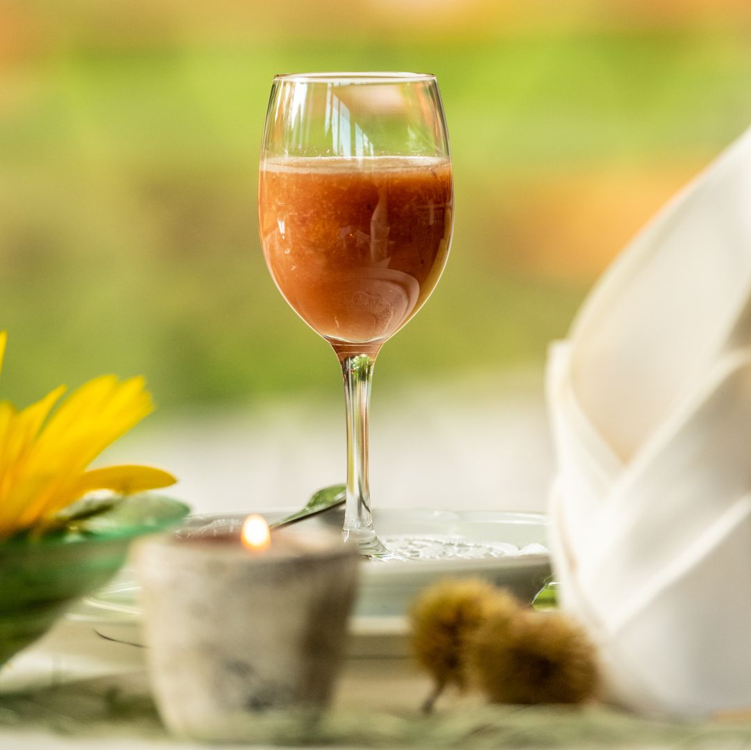 Orangefarbener Smoothie in Weinglas mit Sonnenblume und Kerze