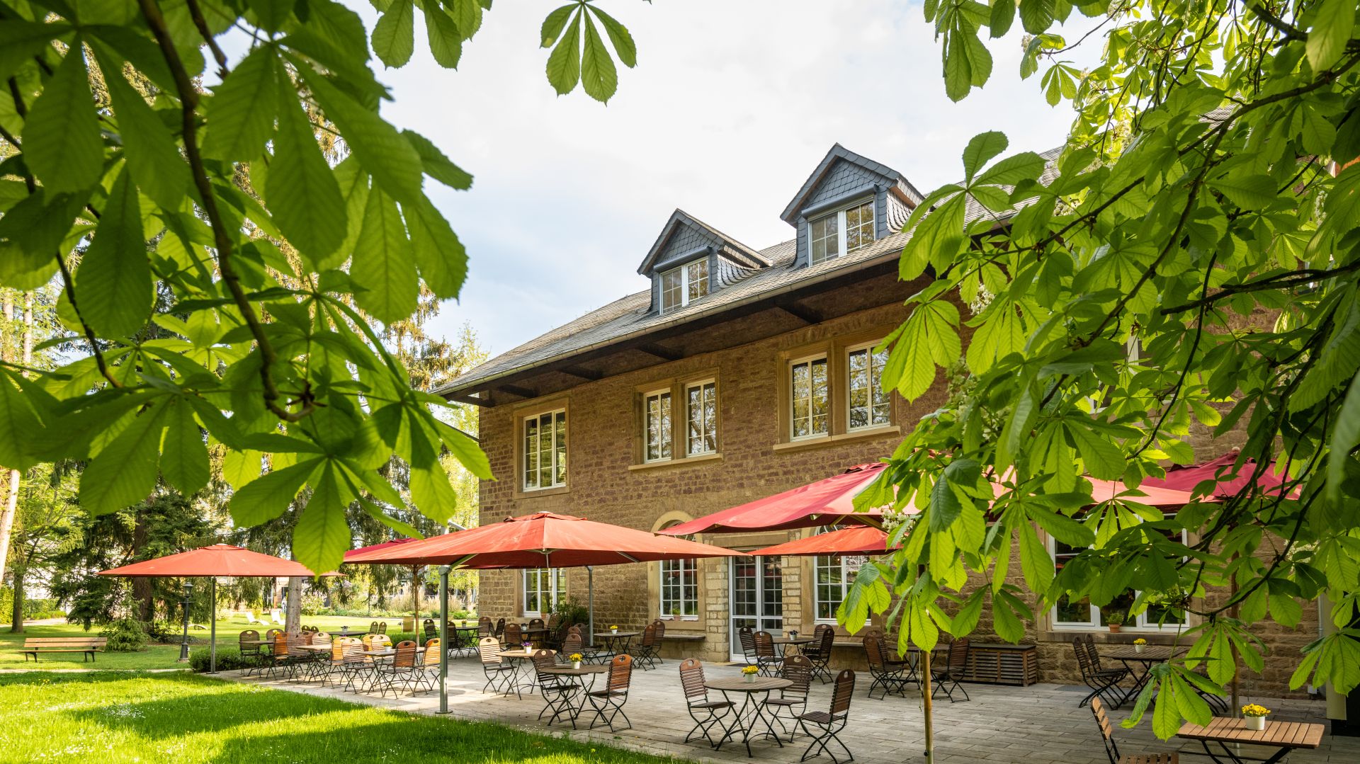 Outdoor cafe patio with red umbrellas in front of a stone building
