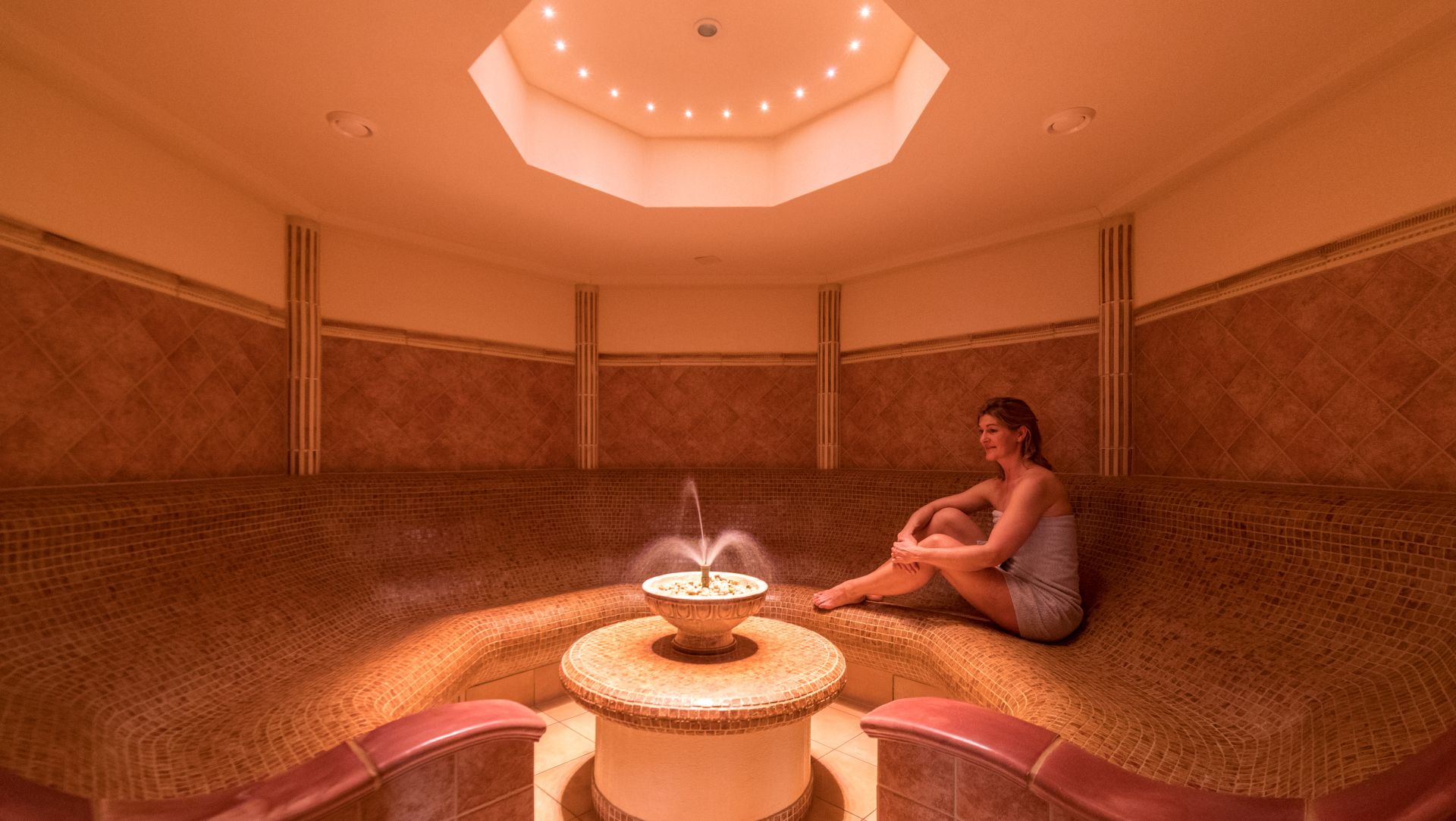 Relaxing person in warm, dimly lit hammam with central fountain and mosaic tiles