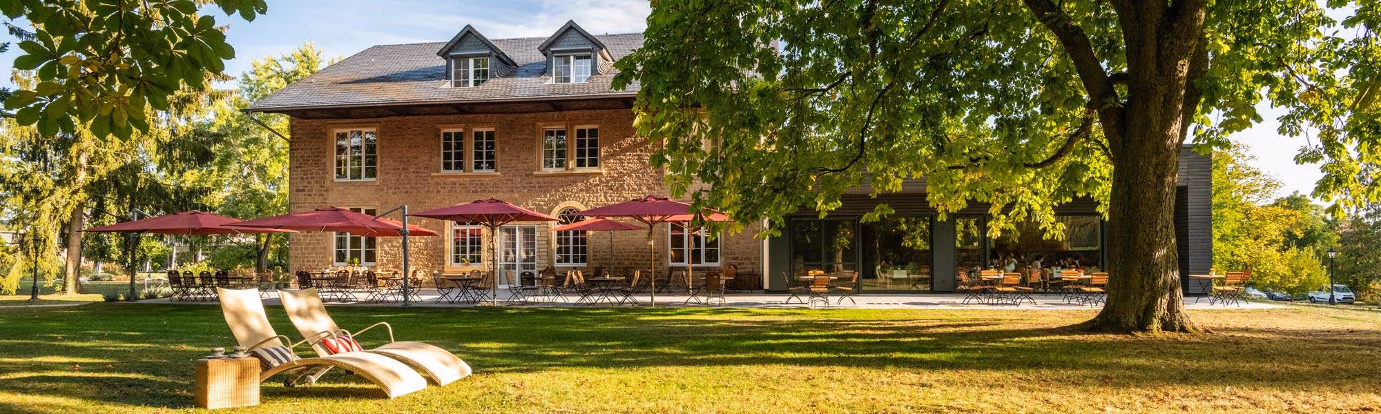 Haupthaus des Vitalresorts mit roten Sonnenschirmen und Liegestühlen im grünen Garten