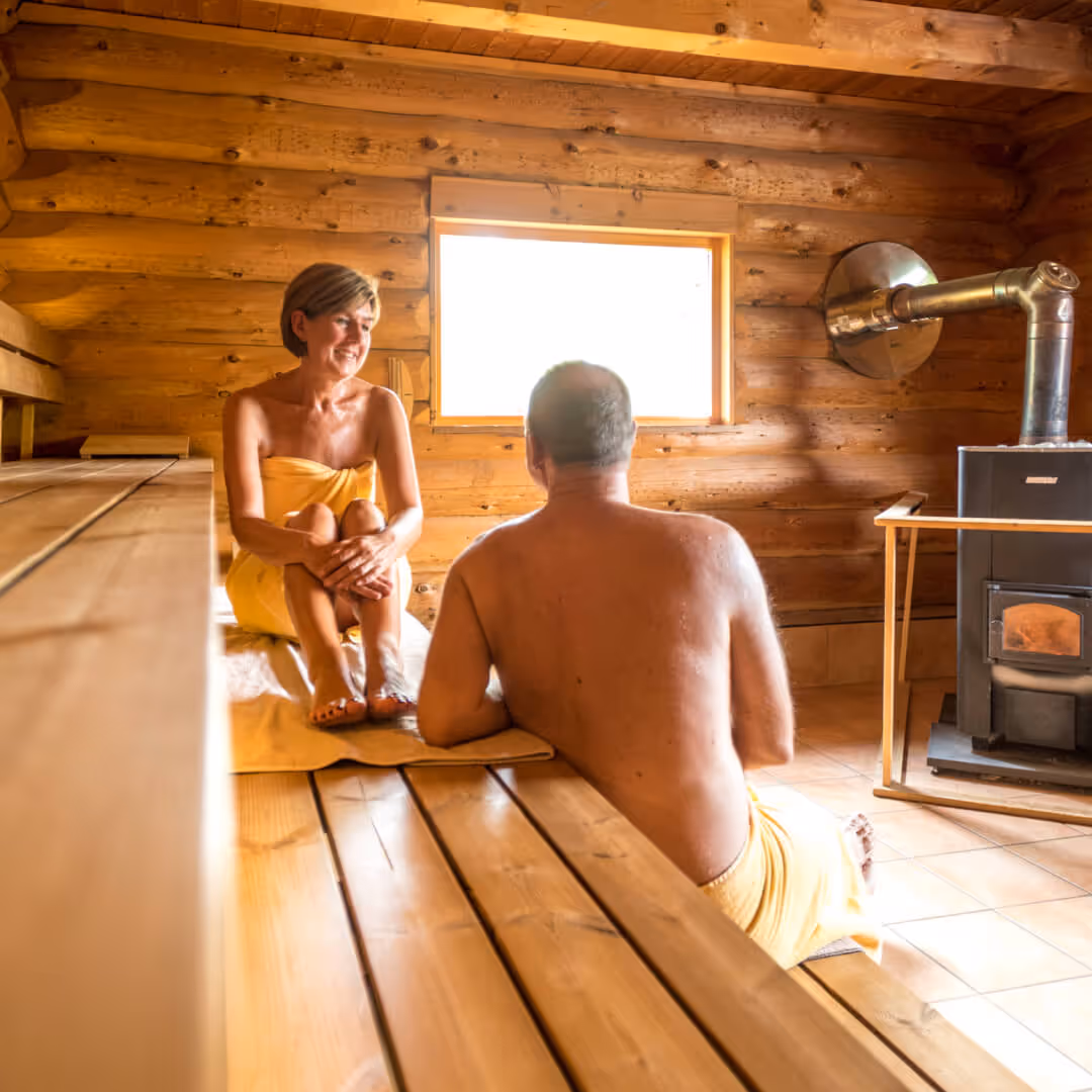 Two people relaxing in a wooden sauna, wrapped in yellow towels