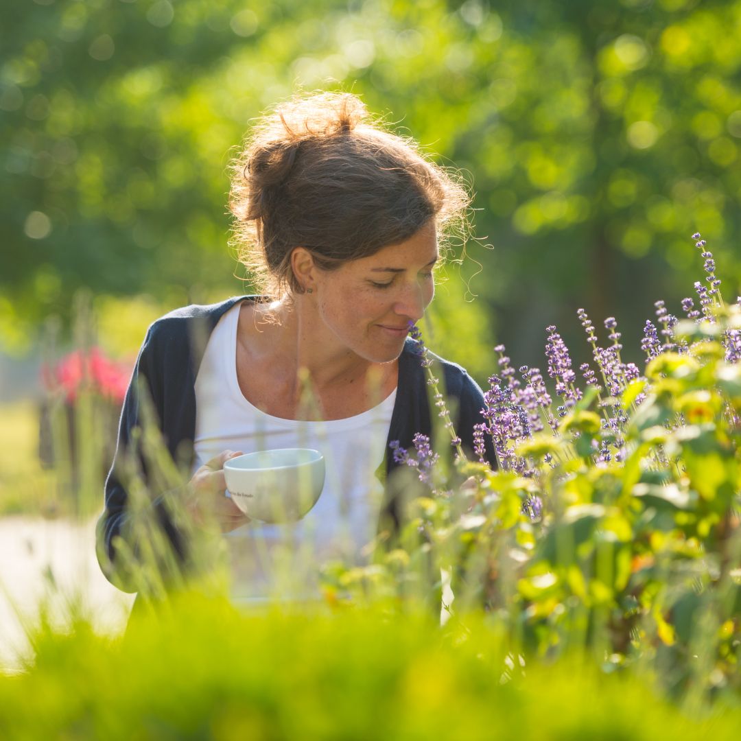 Frau genießt Kaffee zwischen Lavendelblüten im sonnigen Garten