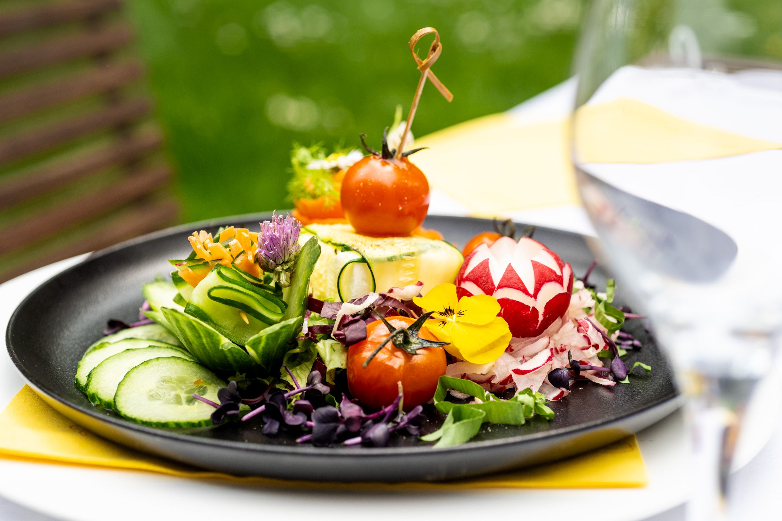 Bunter Salatteller mit Tomaten, Gurken, Blumen und kunstvoller Dekoration