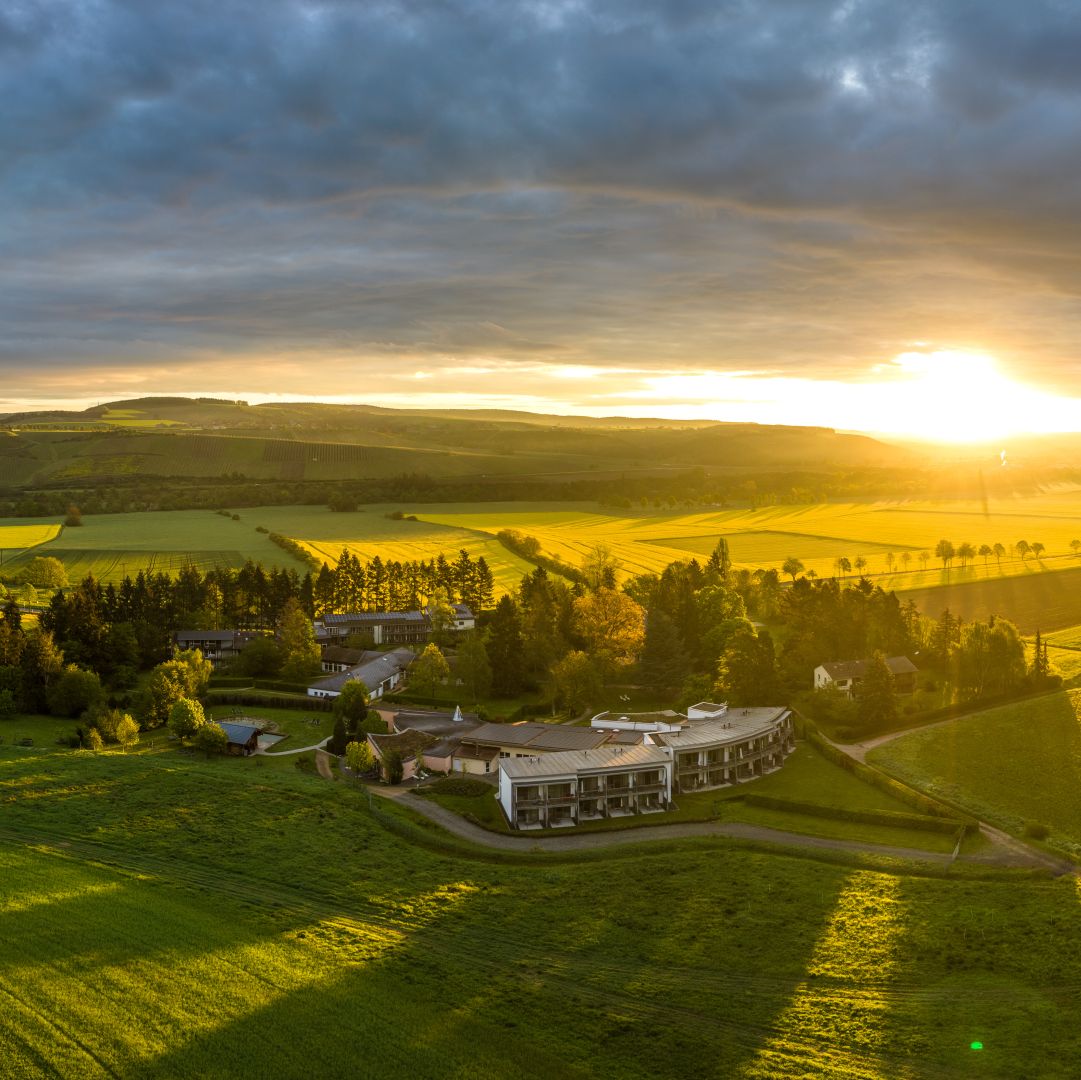 Sunrise over rolling green fields with modern buildings nestled in landscape