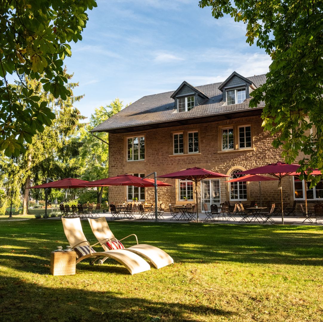Landhaus mit roten Sonnenschirmen und Liegestühlen im grünen Garten