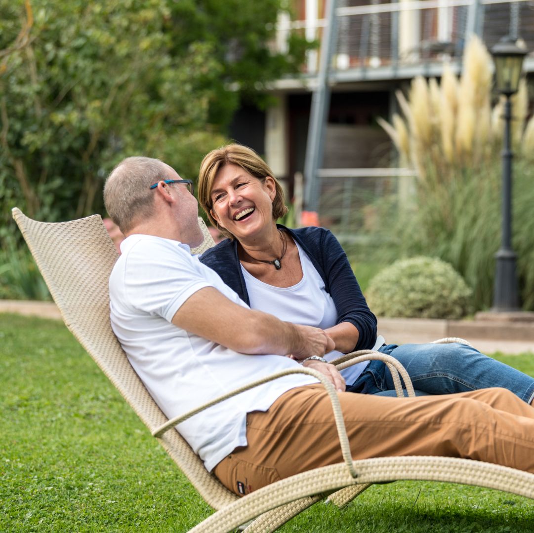 Zwei Personen lachen zusammen auf einem Gartenstuhl im Freien
