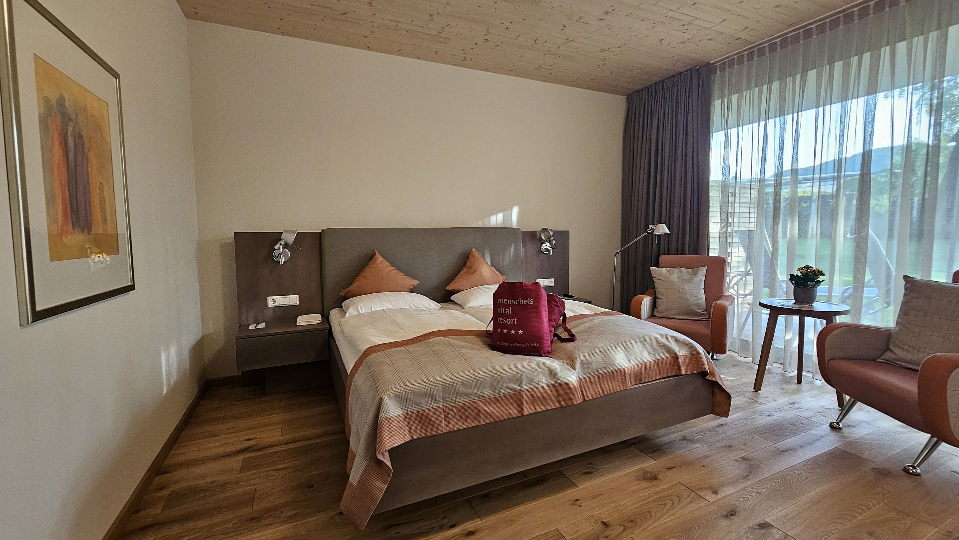 Gemütliches Hotelzimmer mit Bett, Sessel und Bergblick durch Vorhänge