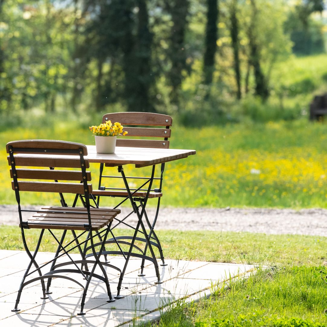 Gartensitzgruppe mit gelben Blumen auf Tisch in sonniger Waldlichtung