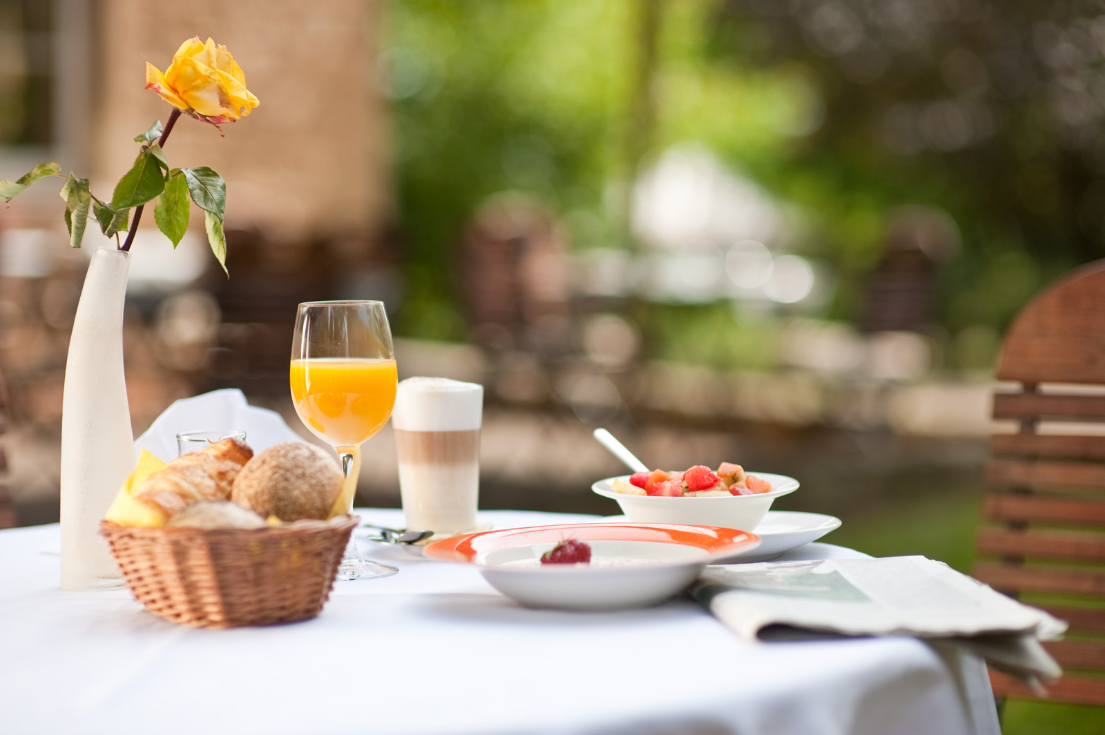 Gedeckter Frühstückstisch mit Croissants, Orangensaft und gelber Rose