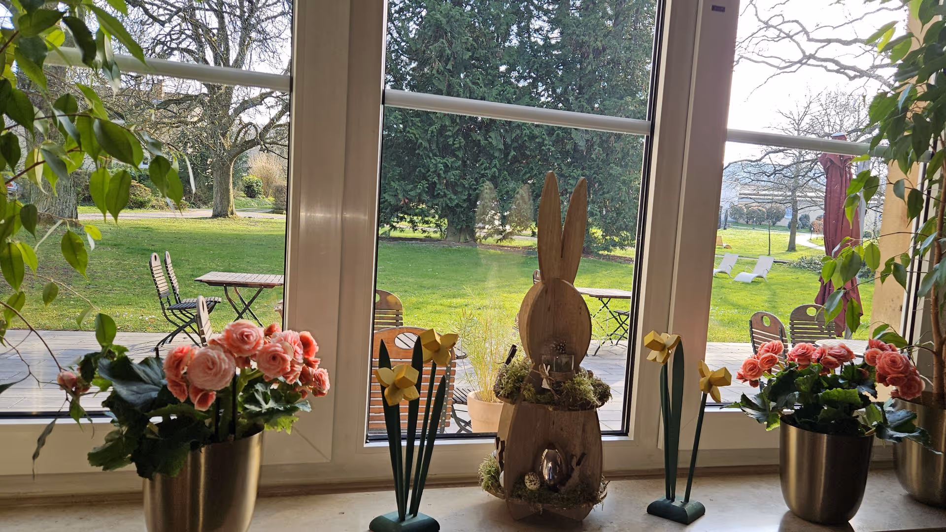 Easter scene with wooden bunny, pink roses, and garden view through window