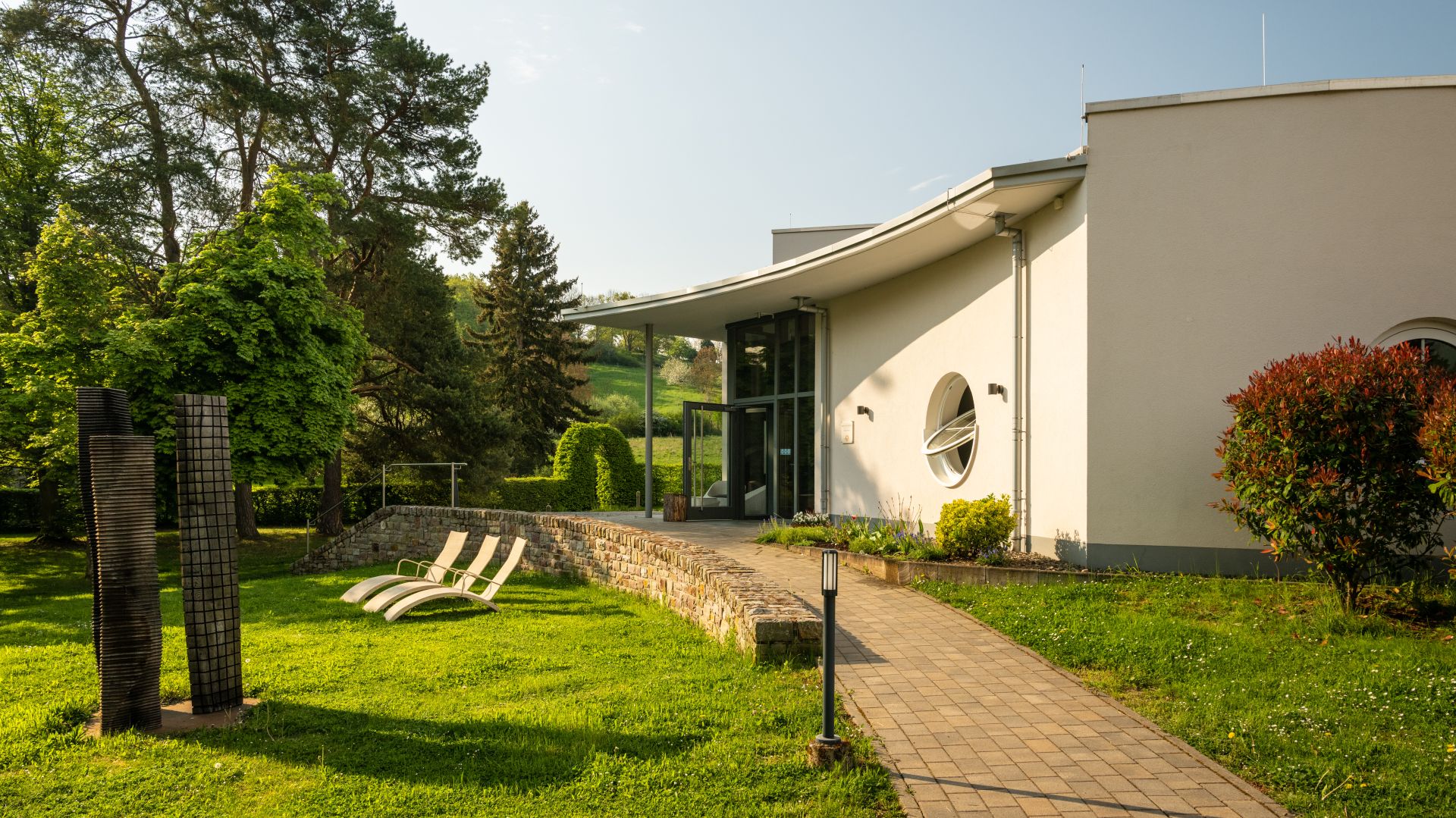 Modernes Gebäude mit Liegestühlen im sonnigen Garten mit Bäumen