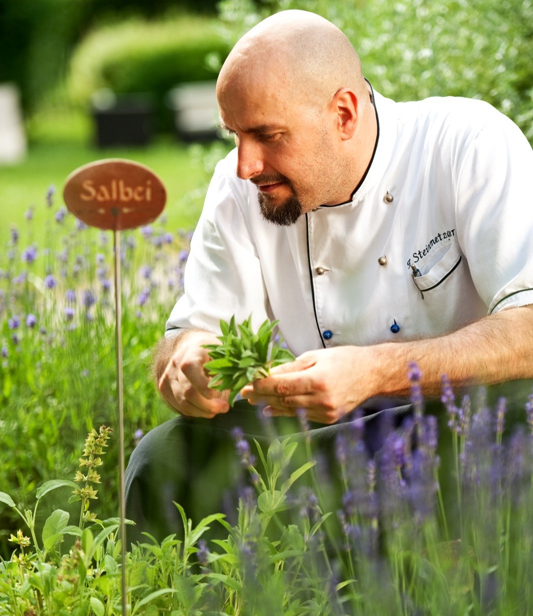 Chef inspecting herbs in lavender garden with Salbei sign nearby
