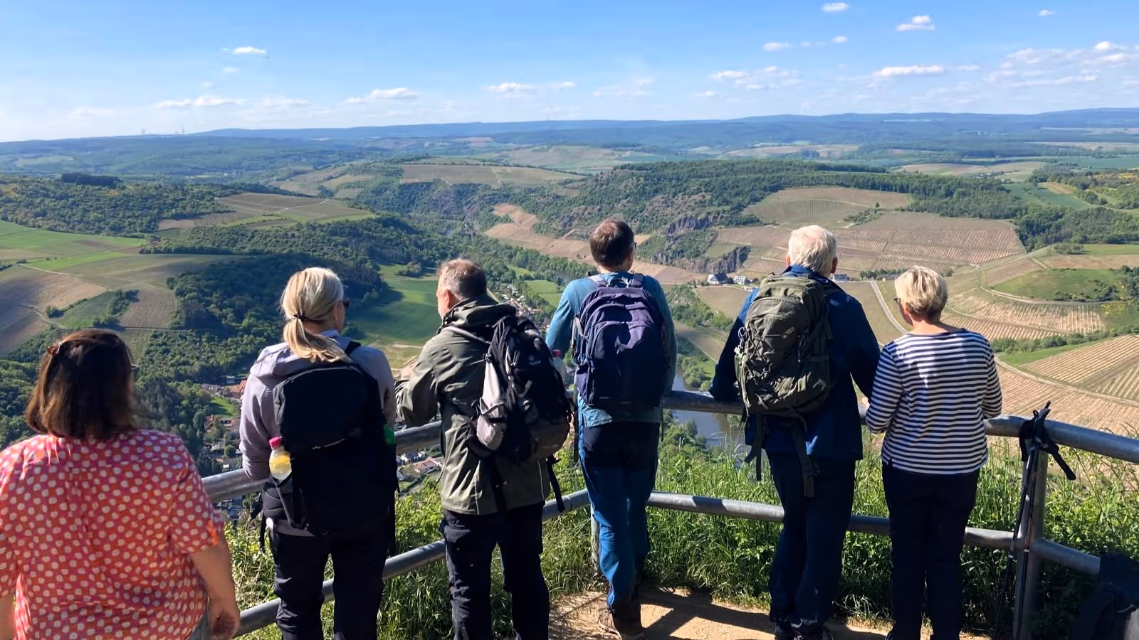 Wandergruppe blickt auf eine weite Landschaft mit Feldern und Wäldern