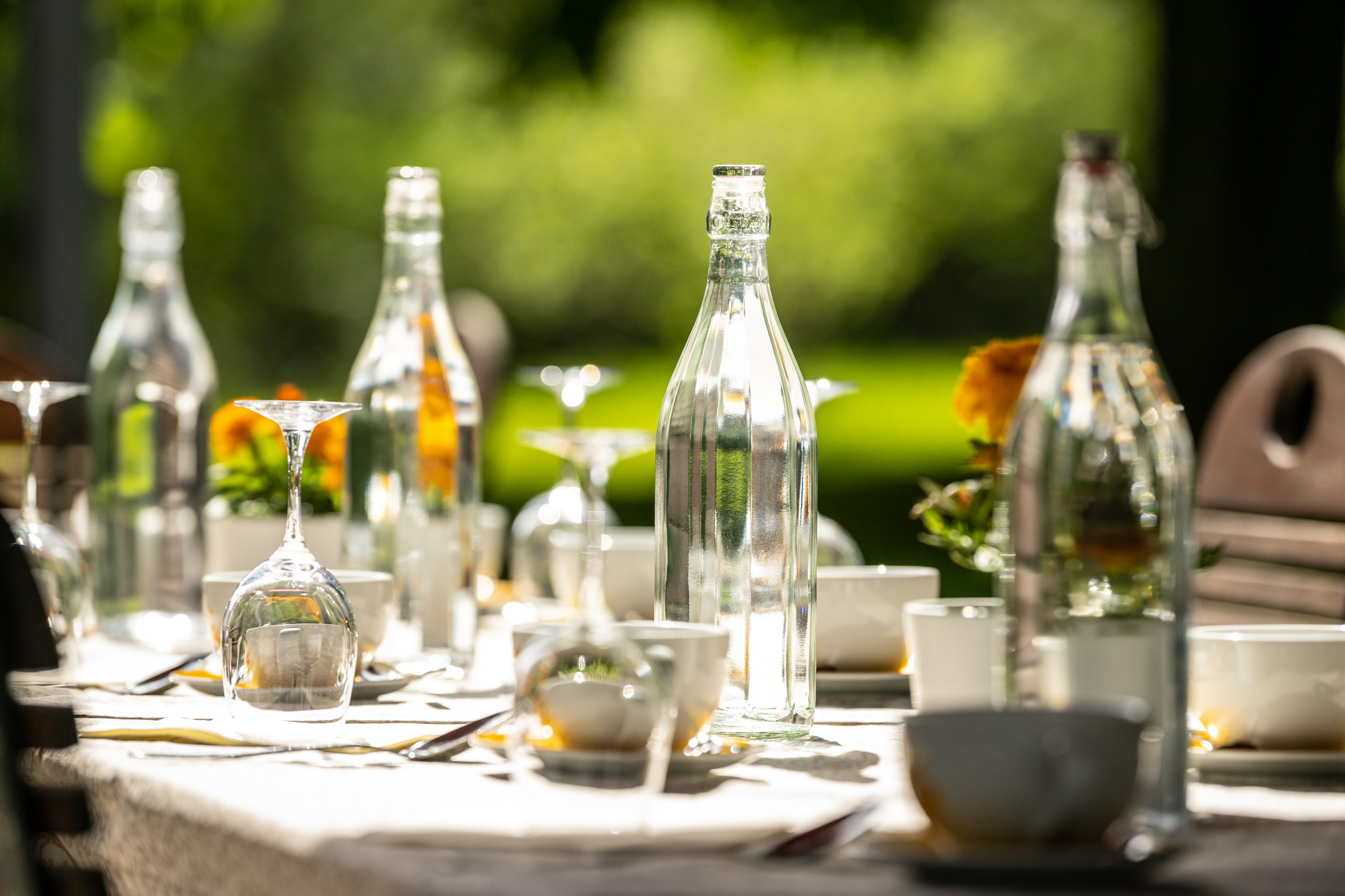 Gedeckter Tisch mit Wassergläsern und Flaschen im Garten