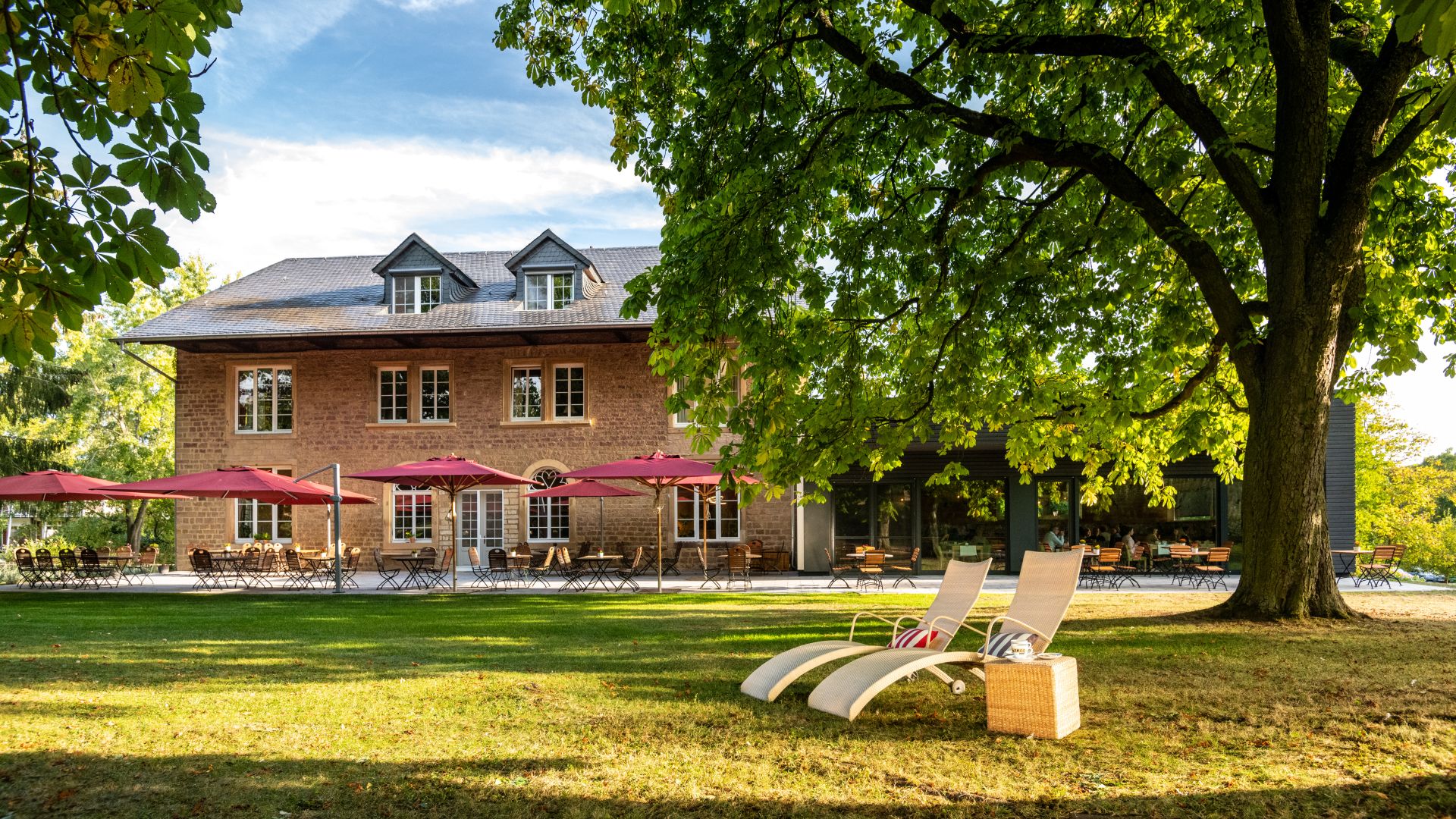 Rustic brick house with red umbrellas, lawn chairs under large tree