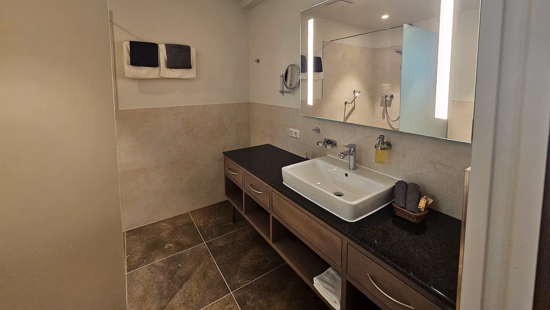 Modern bathroom with wooden vanity, white sink, and neutral stone tiles