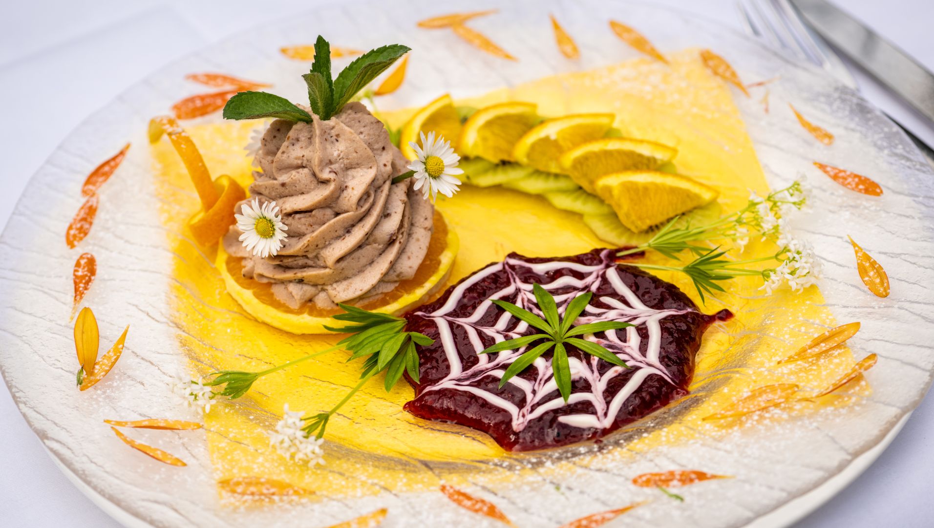 Gourmet dessert with piped cream, berry disk, lemon slices, and flowers