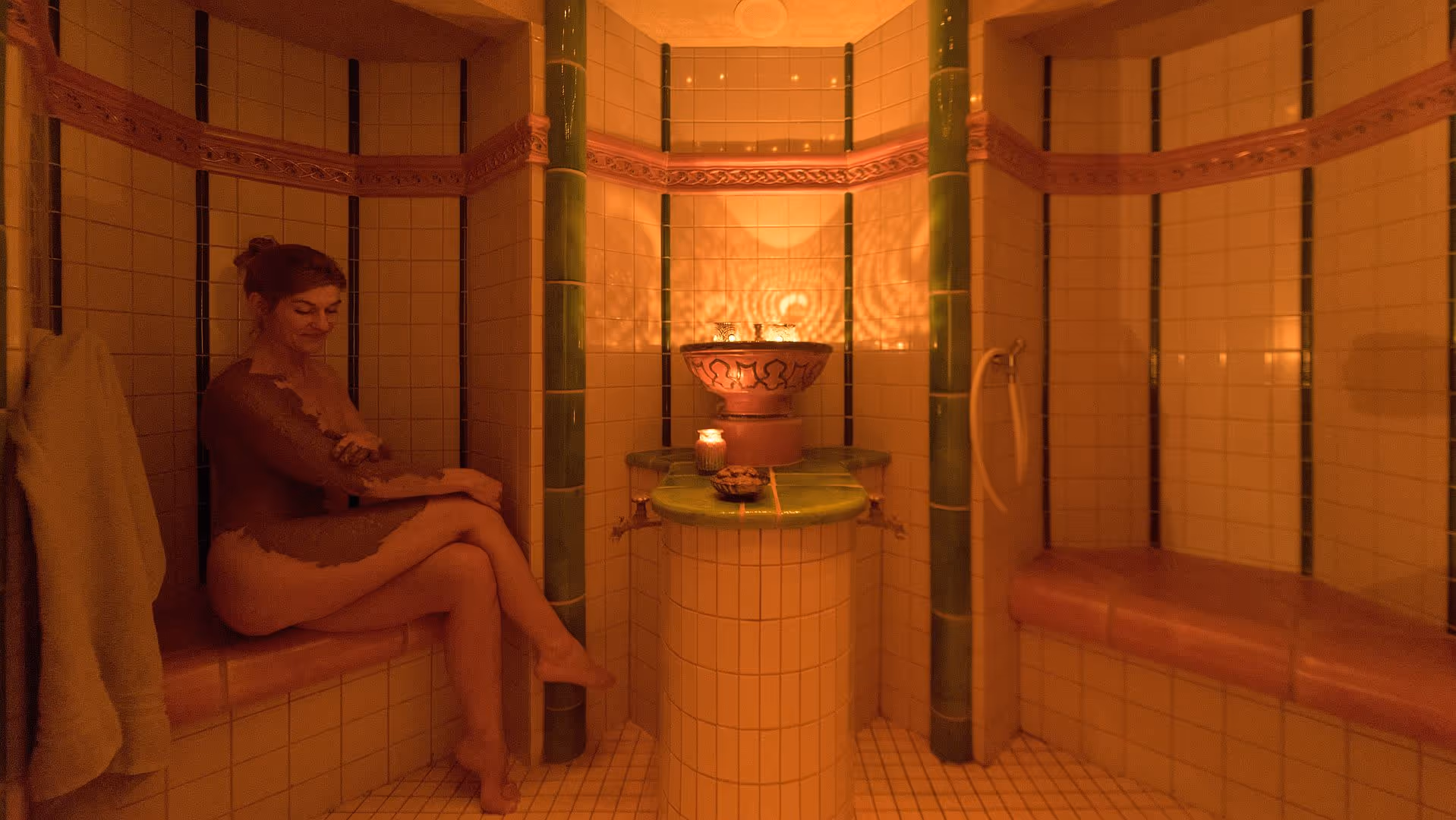 Warm-toned bathroom with ornate tiles, candles, and person relaxing