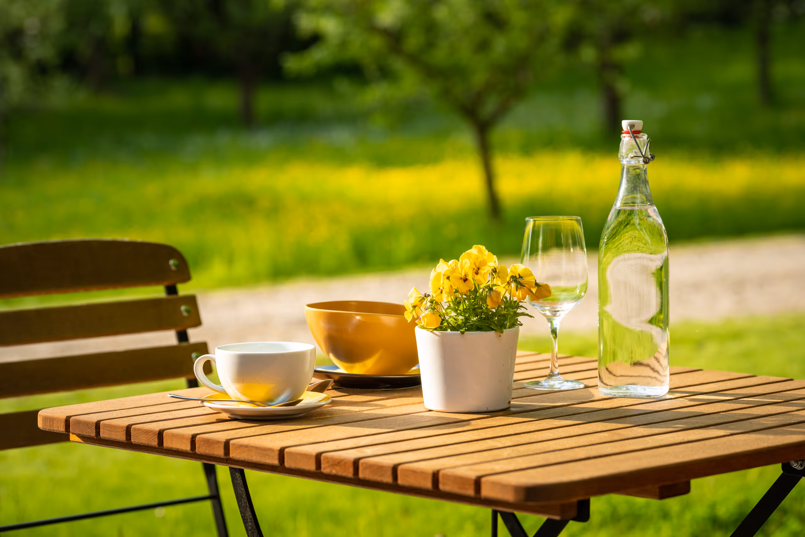Outdoor table with coffee, yellow flowers, water bottle, and garden background